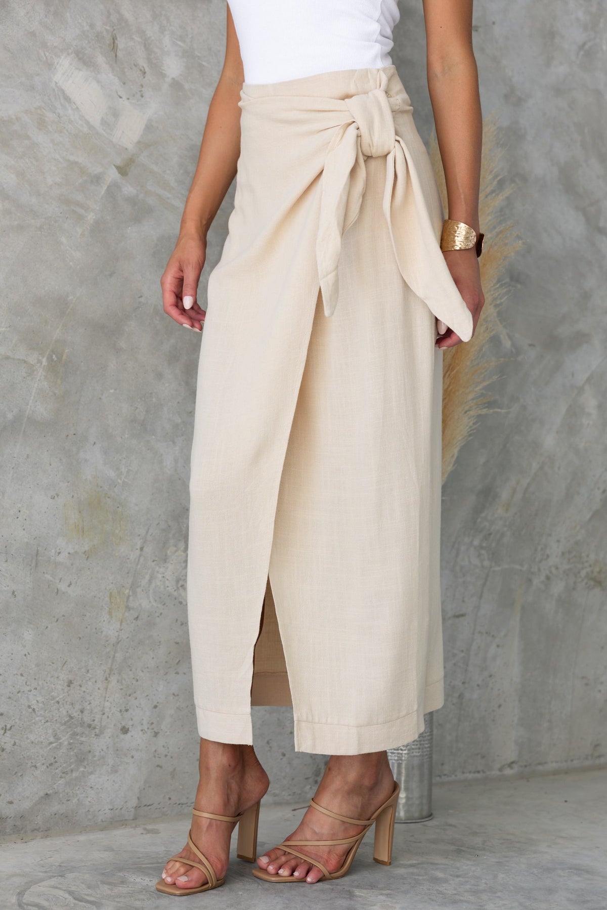 Beige Tahnee Maxi Skirt featuring a wrap design, mid-low waist, tie at side, and asymmetric hemline.