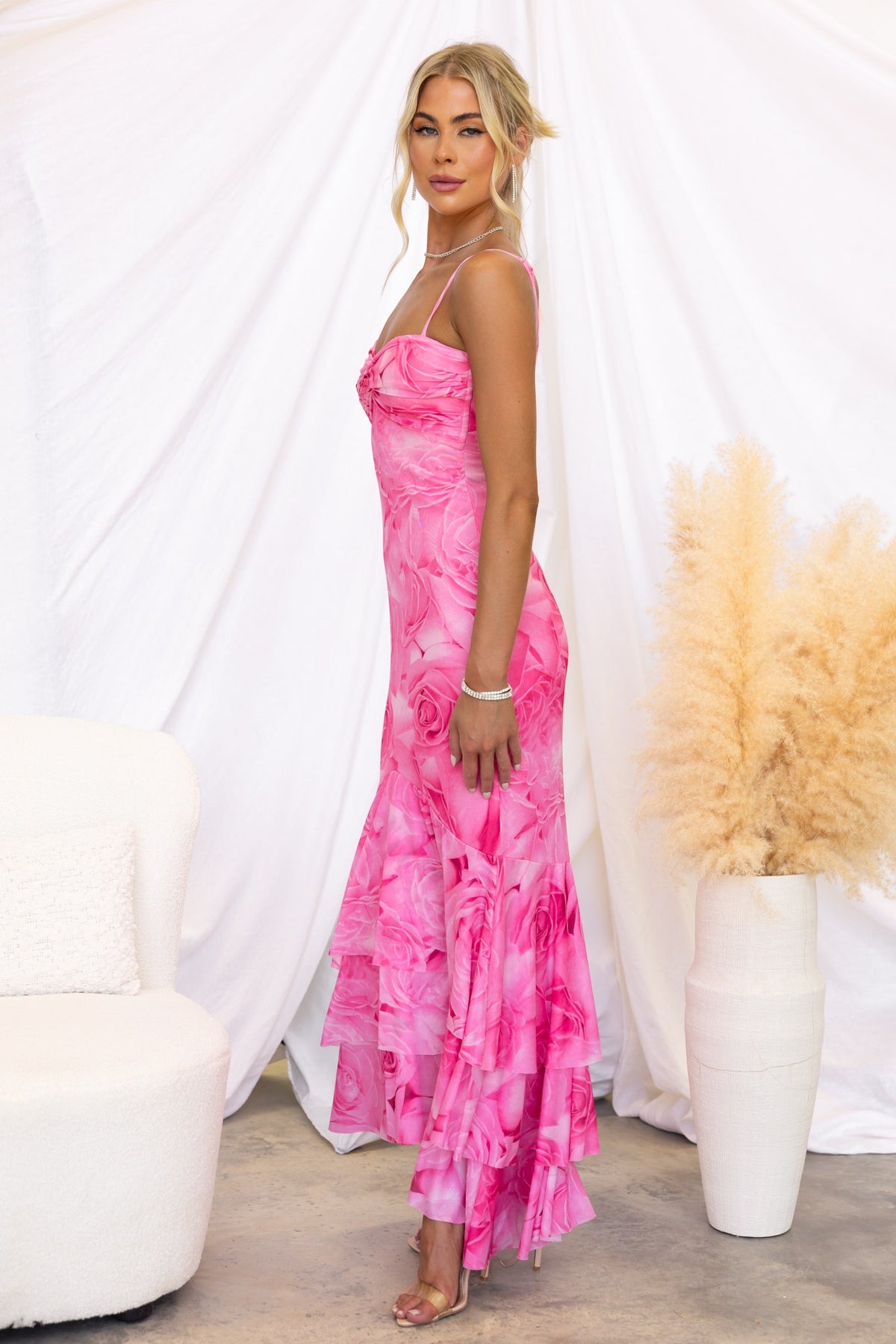 Model wearing Qasila Maxi Dress in pink floral design with a ruffle hem, showcasing adjustable straps and mesh overlay.