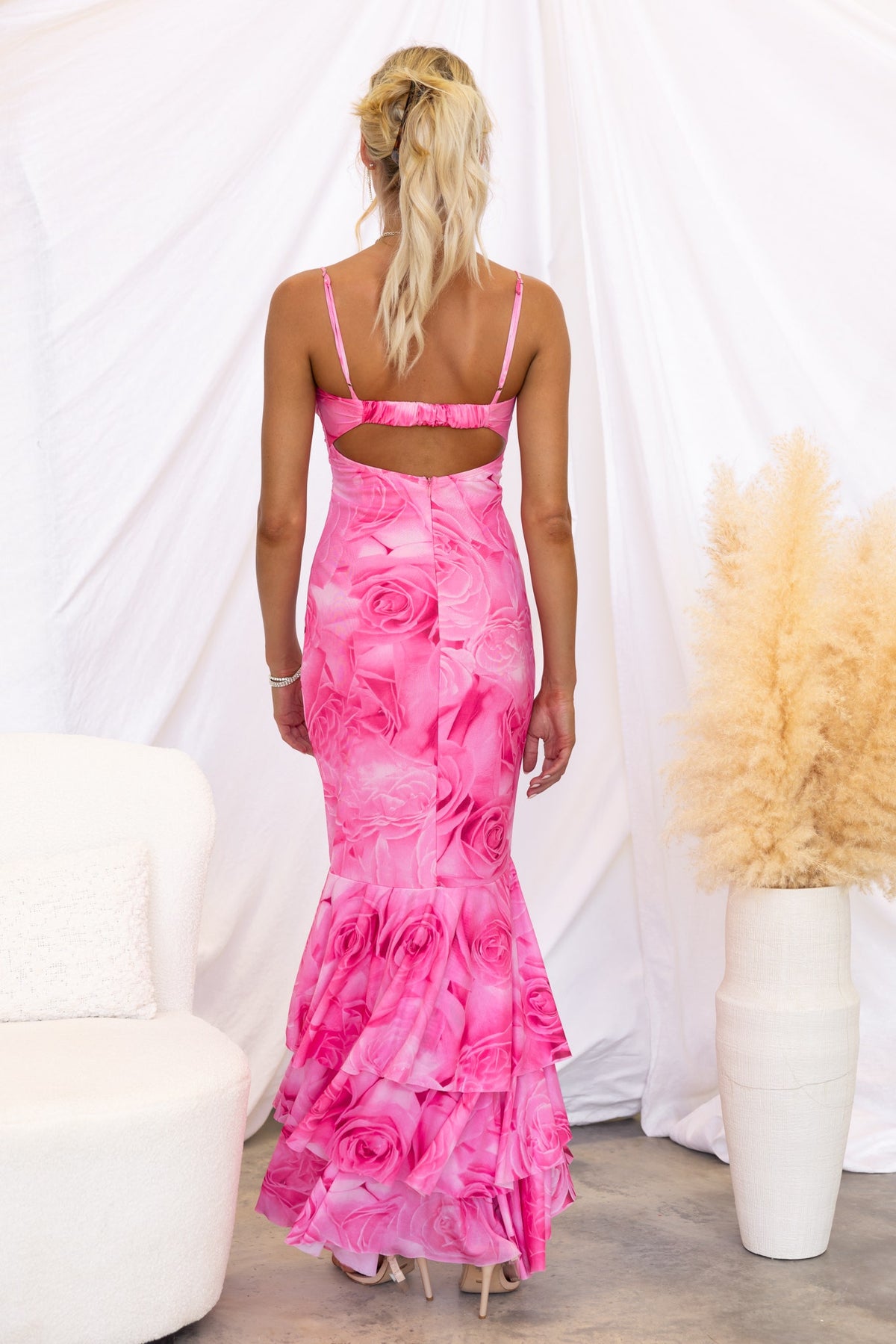 Back view of a woman in a pink floral Qasila maxi dress featuring adjustable straps and ruffle hem.