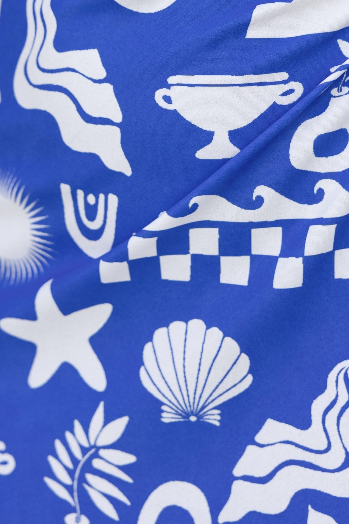 Close-up of abstract blue fabric with white patterns featuring shells, stars, and geometric shapes.