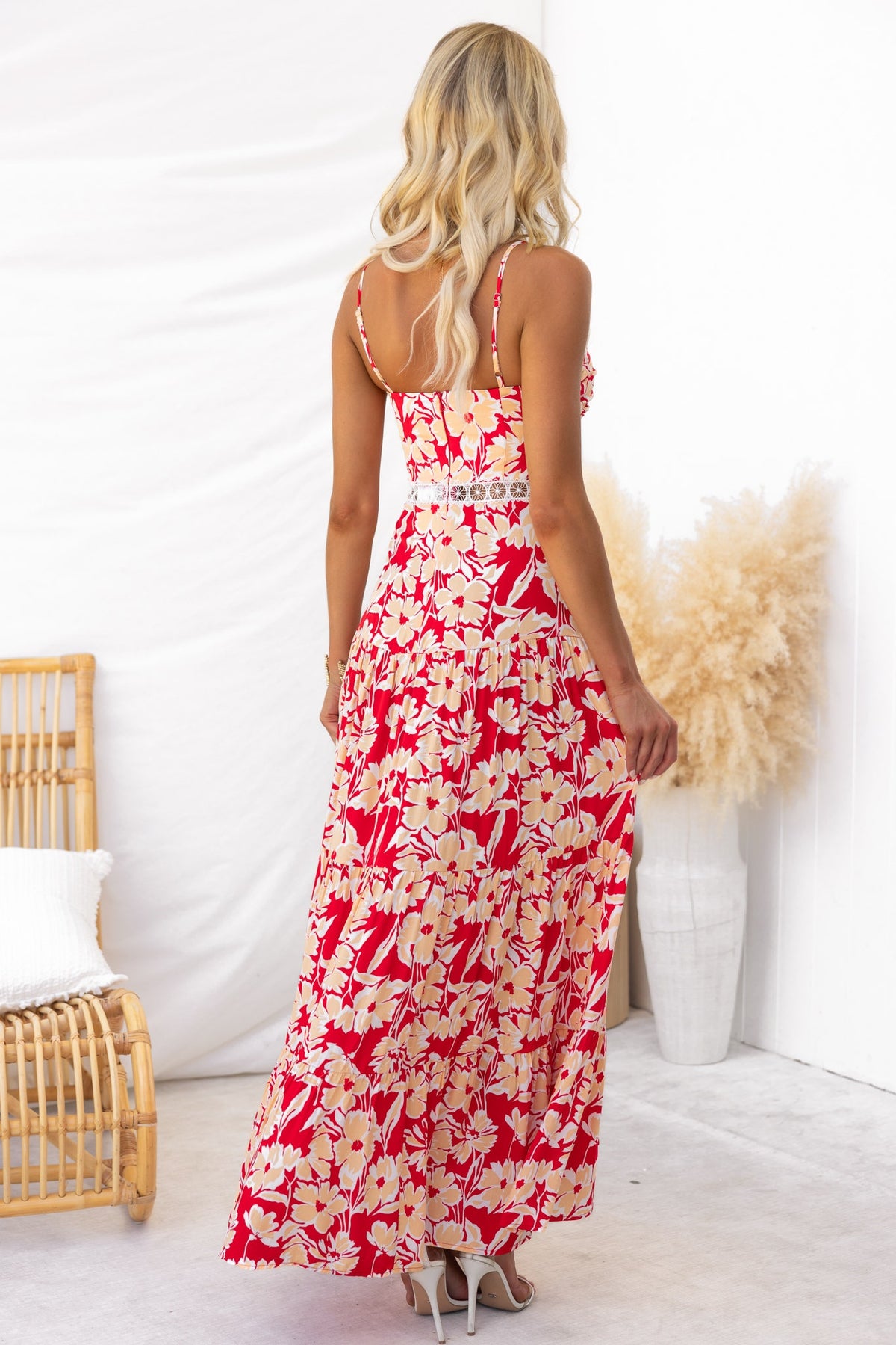 Model wearing red floral print Vani maxi dress with adjustable straps, showing back and lace detail in a bright setting.