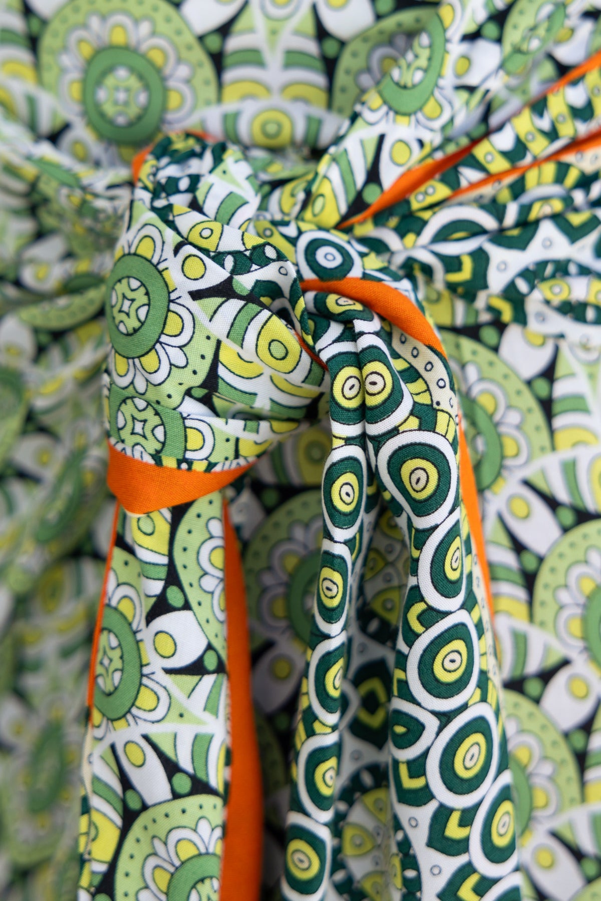 Close-up of Tahnee Maxi Skirt fabric featuring vibrant green and orange patterns with a tied side detail.