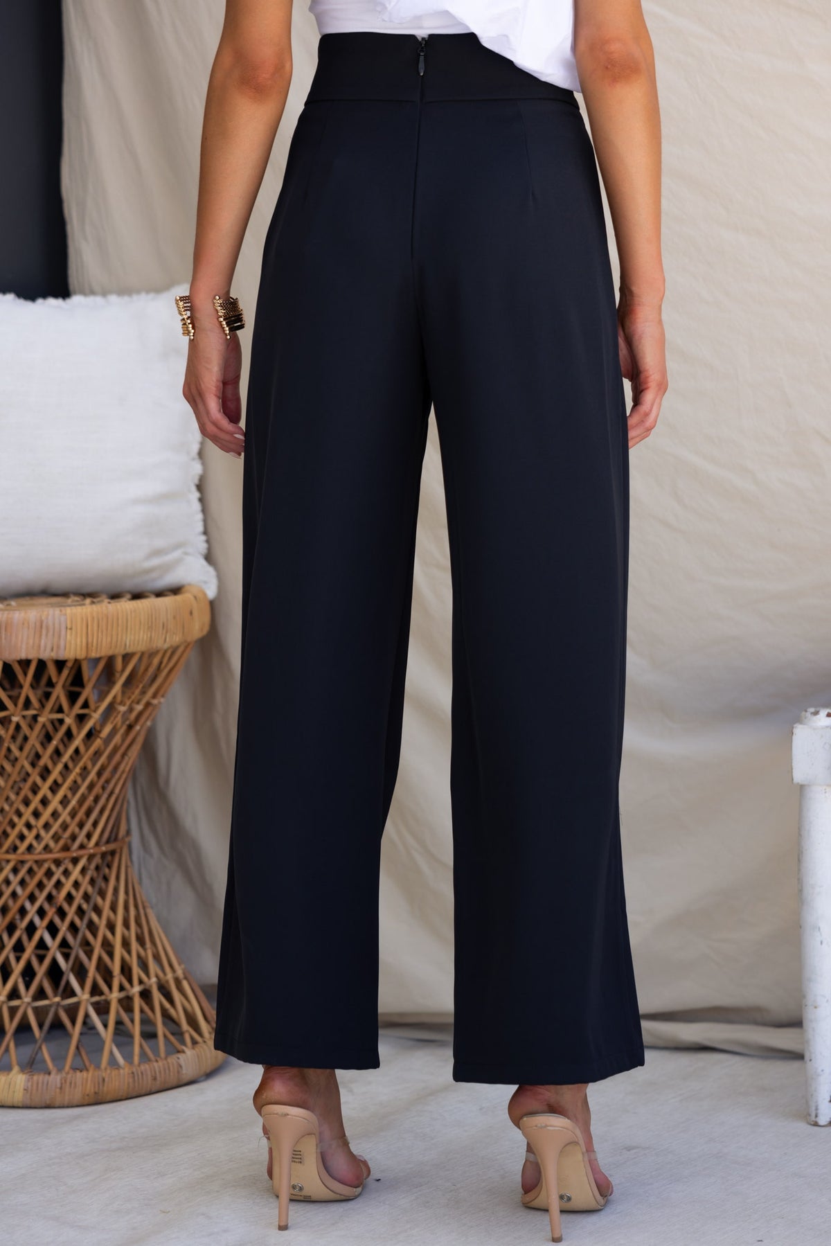 Back view of Lianna black dress pants with mid-high waist and buckle detail, styled with high heels.