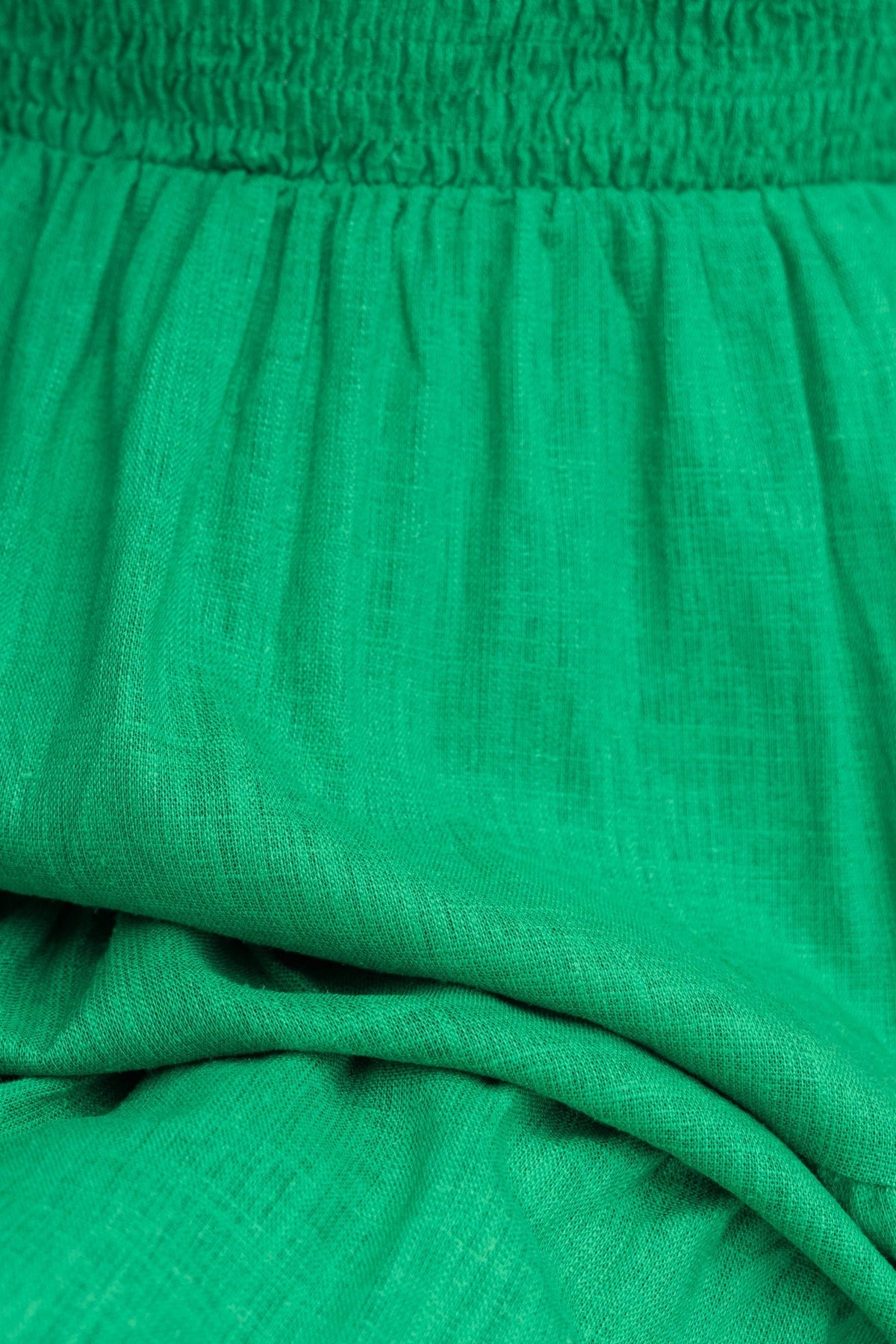 Close-up of green fabric showcasing the smocked waistband and soft linen-like texture of the Alaria Dress.