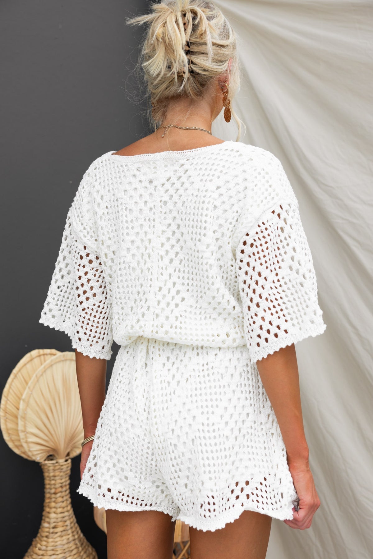 Woman wearing a white crochet Momo Playsuit, showcasing a relaxed fit and open knit design.