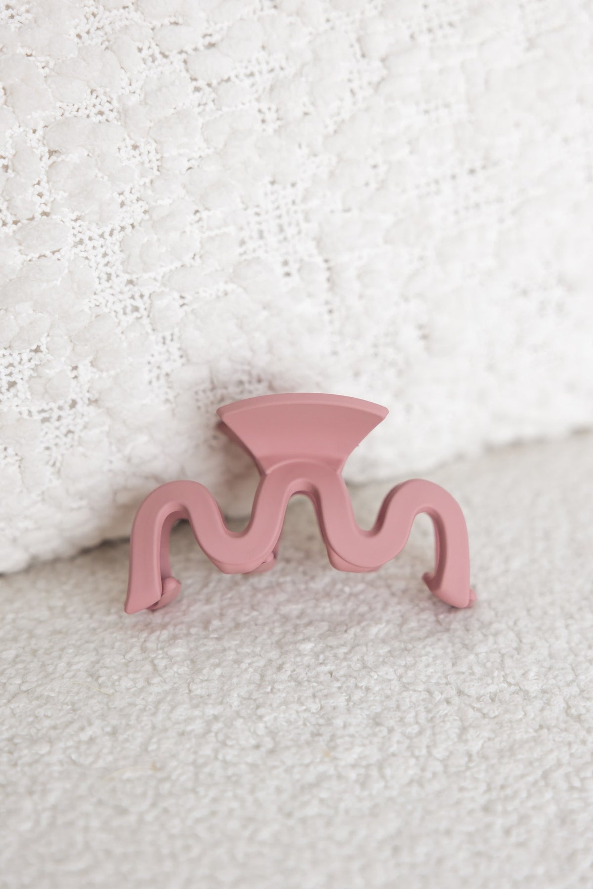 Matte pink Paris claw clip, 8cm in length, resting on soft textured fabric background.