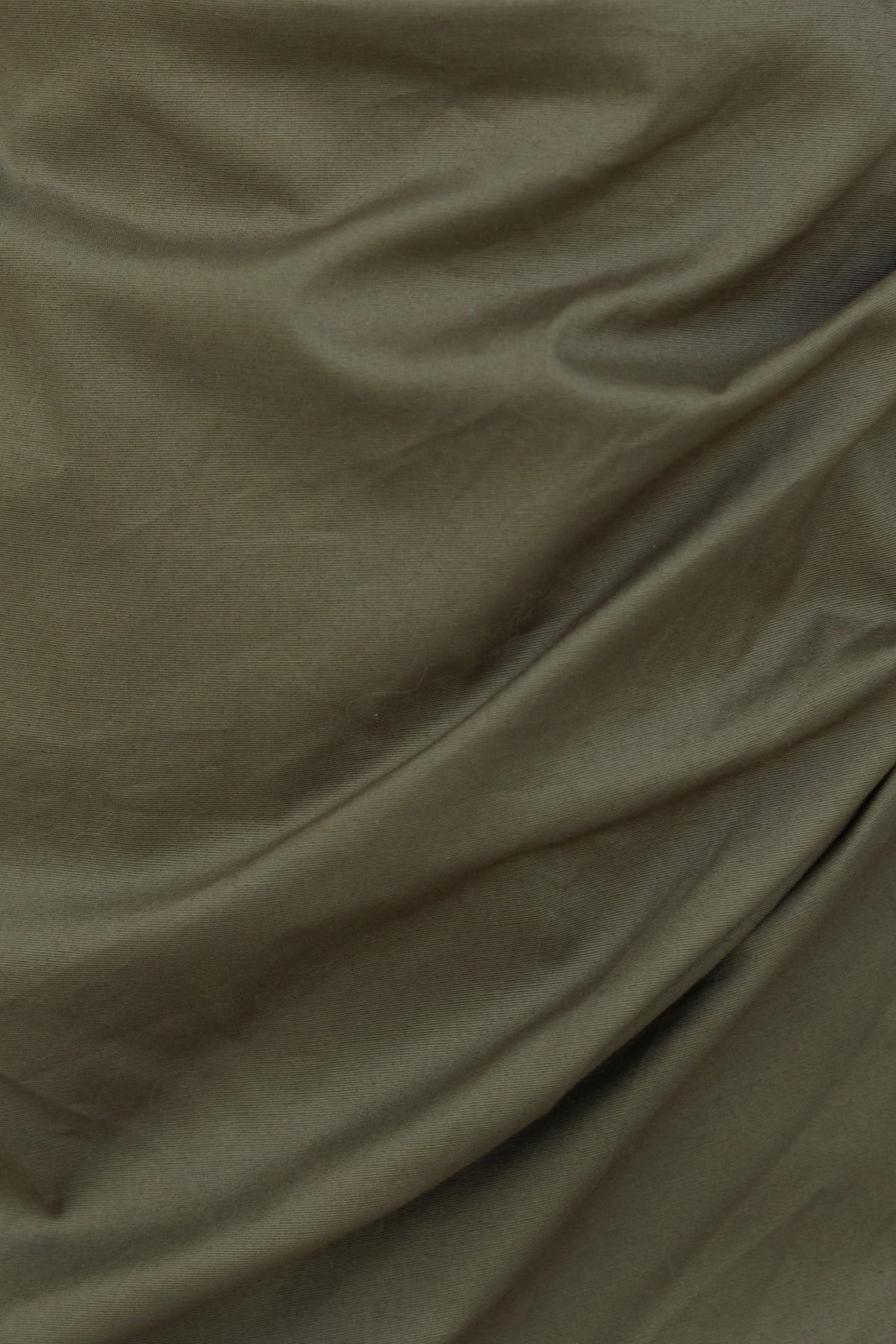 Close-up of olive green fabric with draped texture, showcasing a soft cotton feel for stylish clothing.