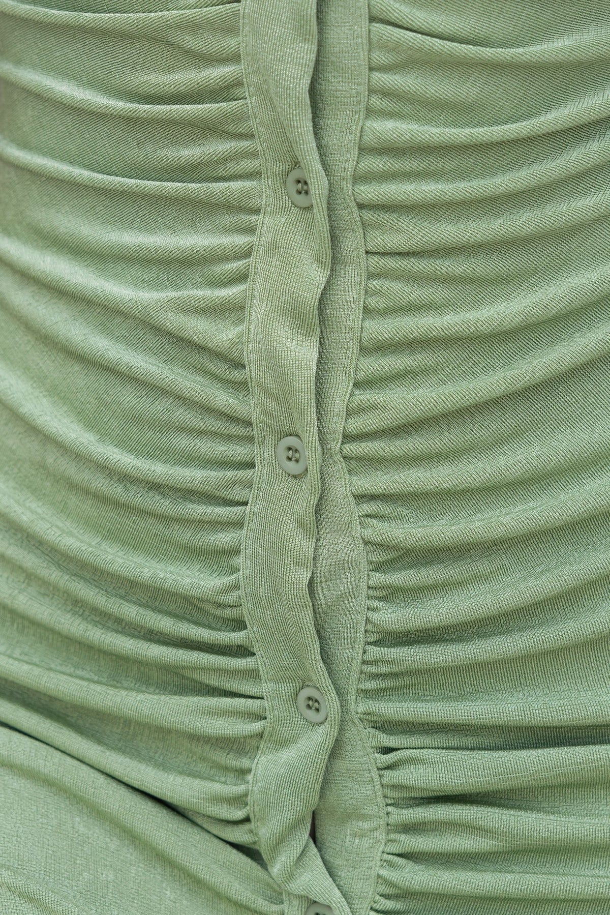 Close-up of the ruched buttons on the Shamine Dress in soft green, showcasing stretchy, slinky fabric.