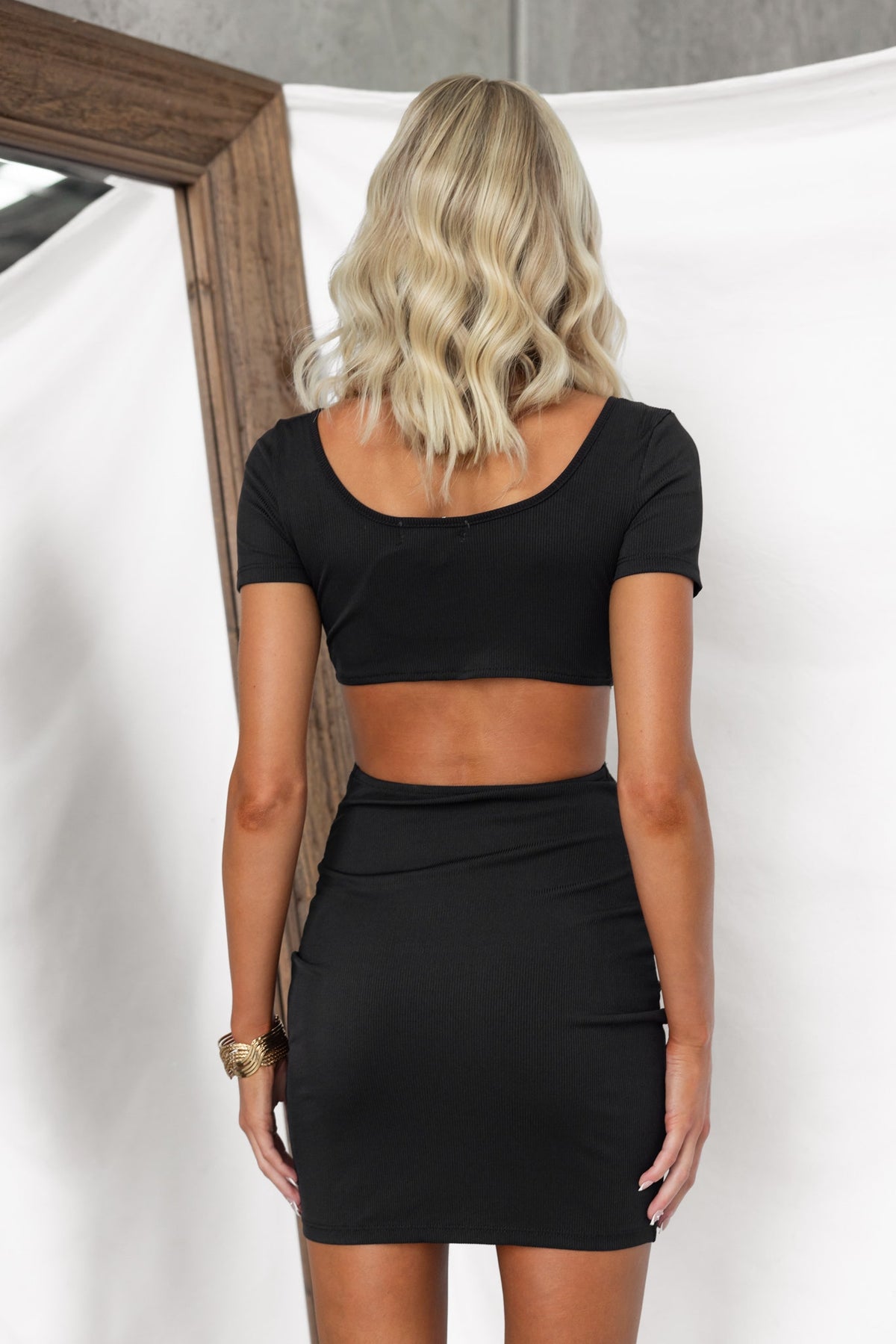 Back view of a model in a black crop top and skirt set, showcasing a stylish and chic look.