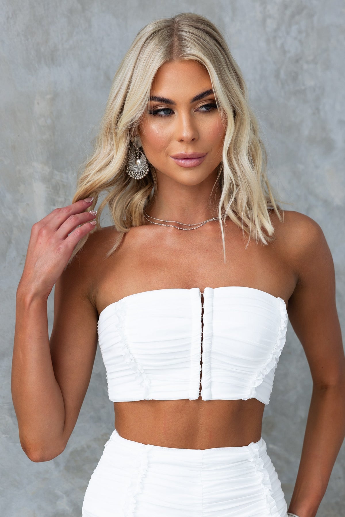Model wearing Deia Top, a strapless white top with front hook fastenings and a ruched design, perfect for a stylish look.