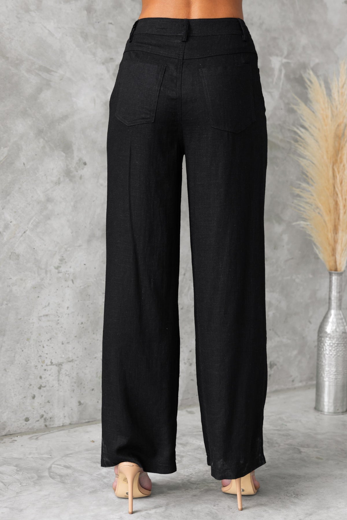 Back view of Aleo Pants featuring a mid-high waist, linen look, and pockets, styled with heels.