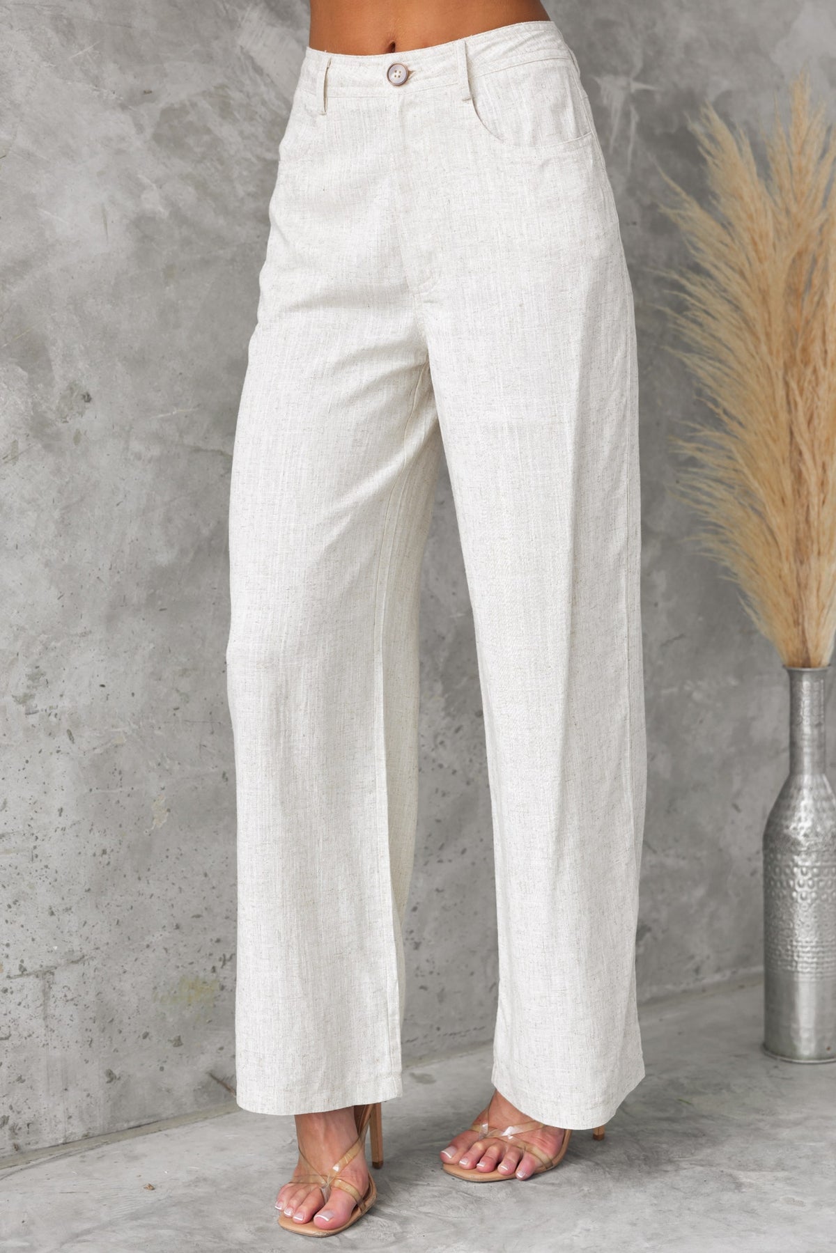 Model wearing Aleo Pants, mid-high waist linen blend, with pockets, in a stylish light color against a textured background.