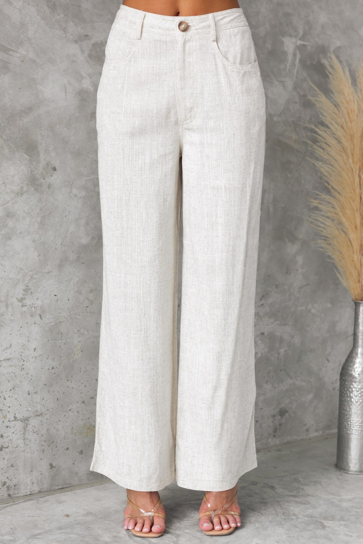Aleo Pants in lightweight beige fabric with thigh-high waist, front and back pockets, styled with sandals.