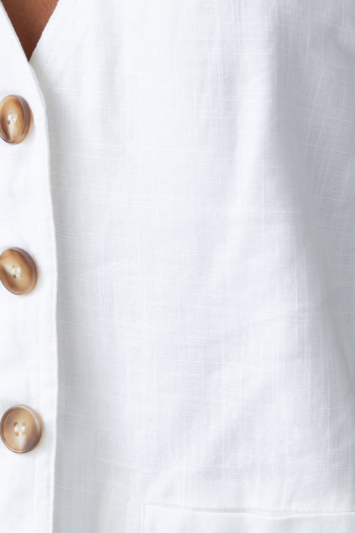 Close-up of white linen fabric with buttons, showcasing textured surface and stylish detail.