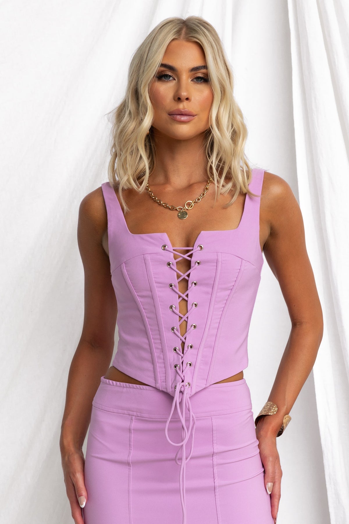 Theon Top in lavender featuring a square neckline and lace-up front, styled with a fitted skirt.