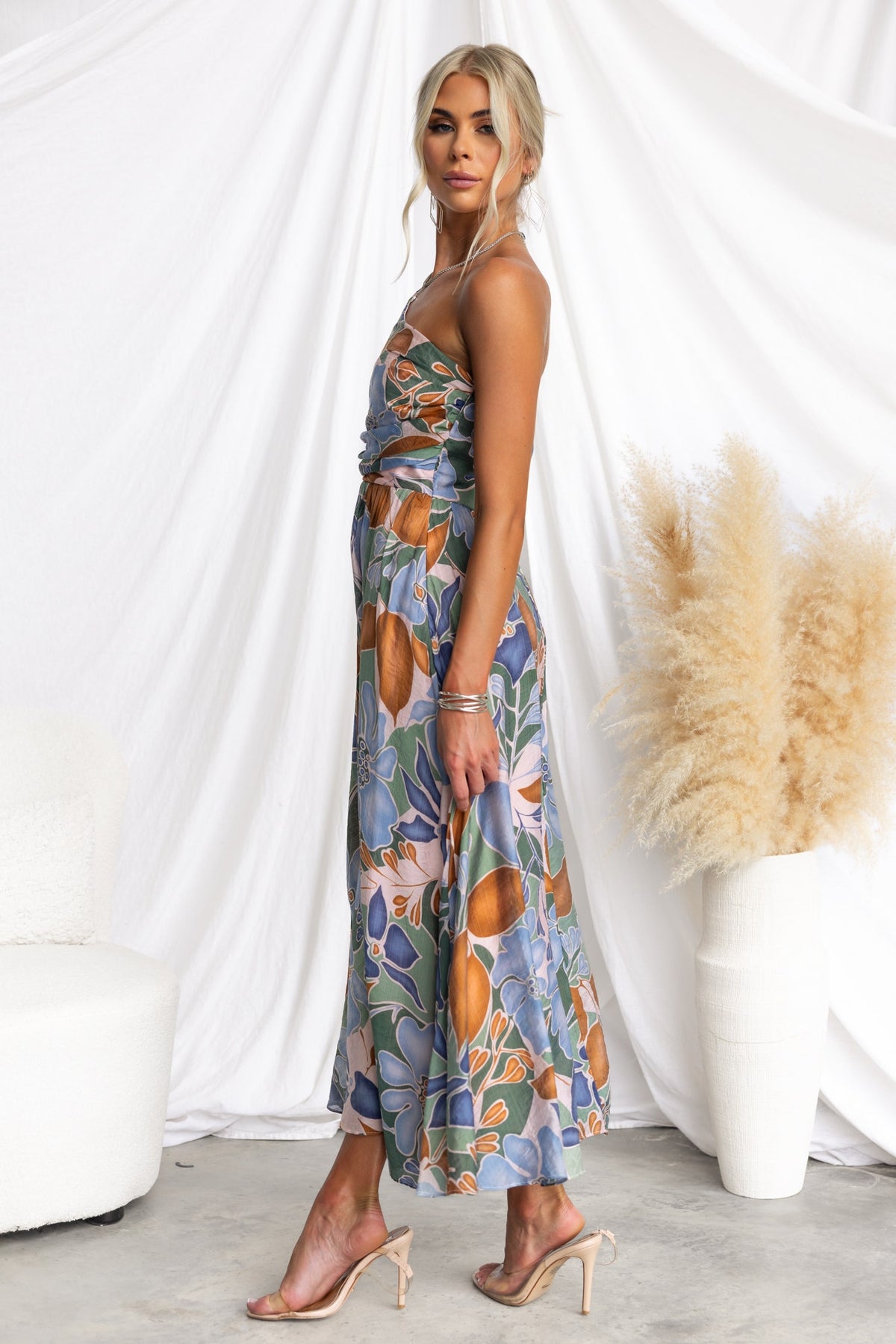 Model wearing Woran Midi Dress, featuring floral print, one-shoulder neckline, styled with strappy heels.