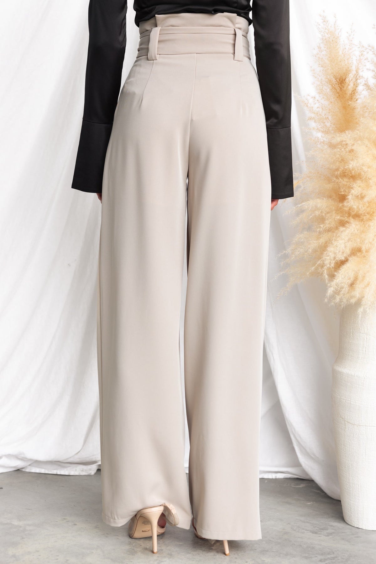 Back view of Jaspin Pants featuring a paper bag waist, removable tie, and wide legs in a light beige color.