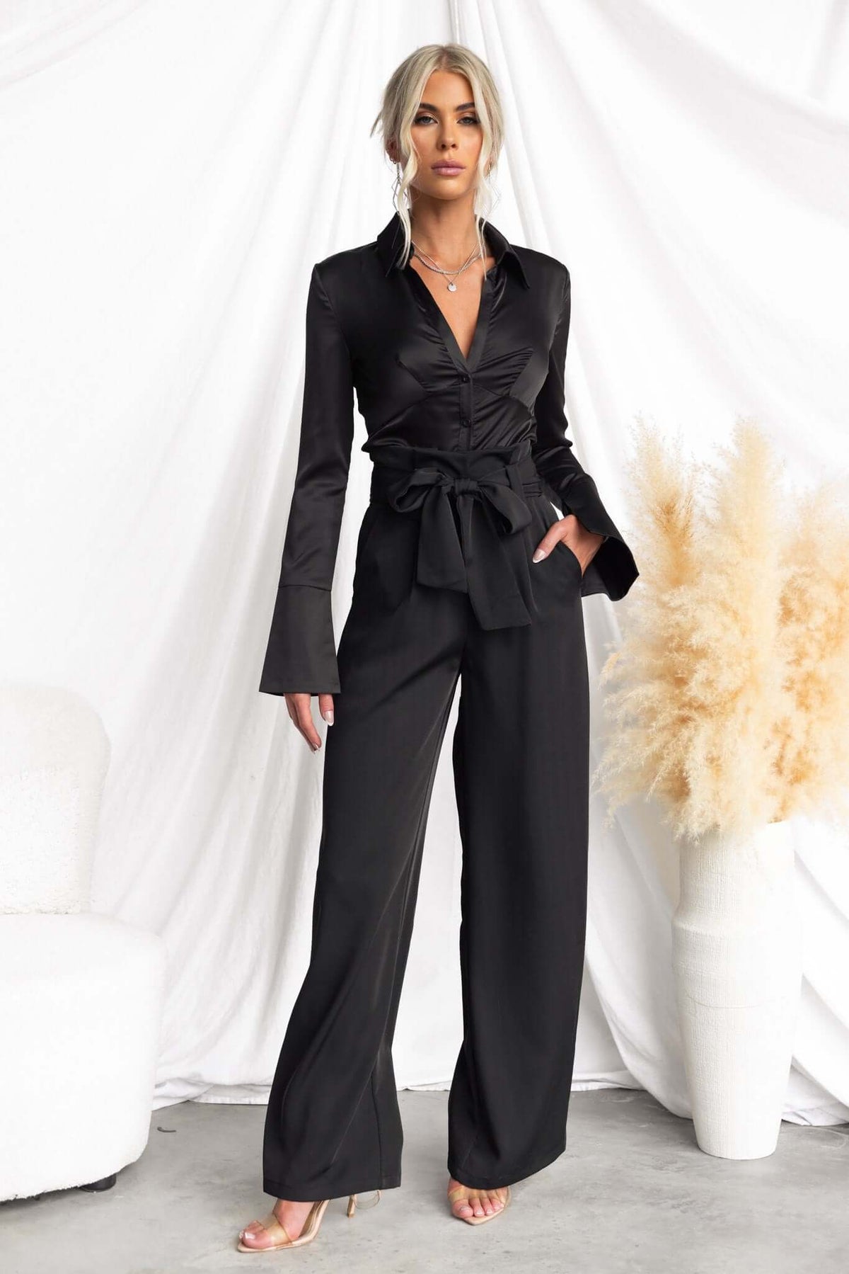 Model wearing Jaspin Pants, a chic black outfit with a paper bag waist, wide legs, and stylish tie detail.
