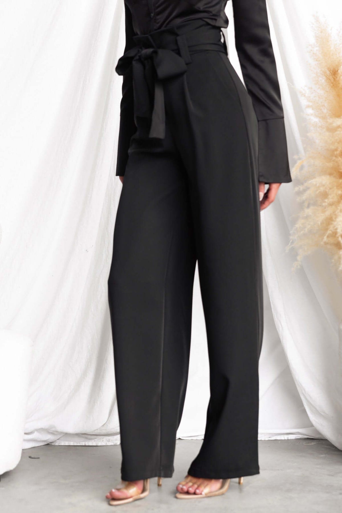 Black Jaspin pants with a paper bag waist and removable tie, featuring wide legs and pockets, worn by a model.
