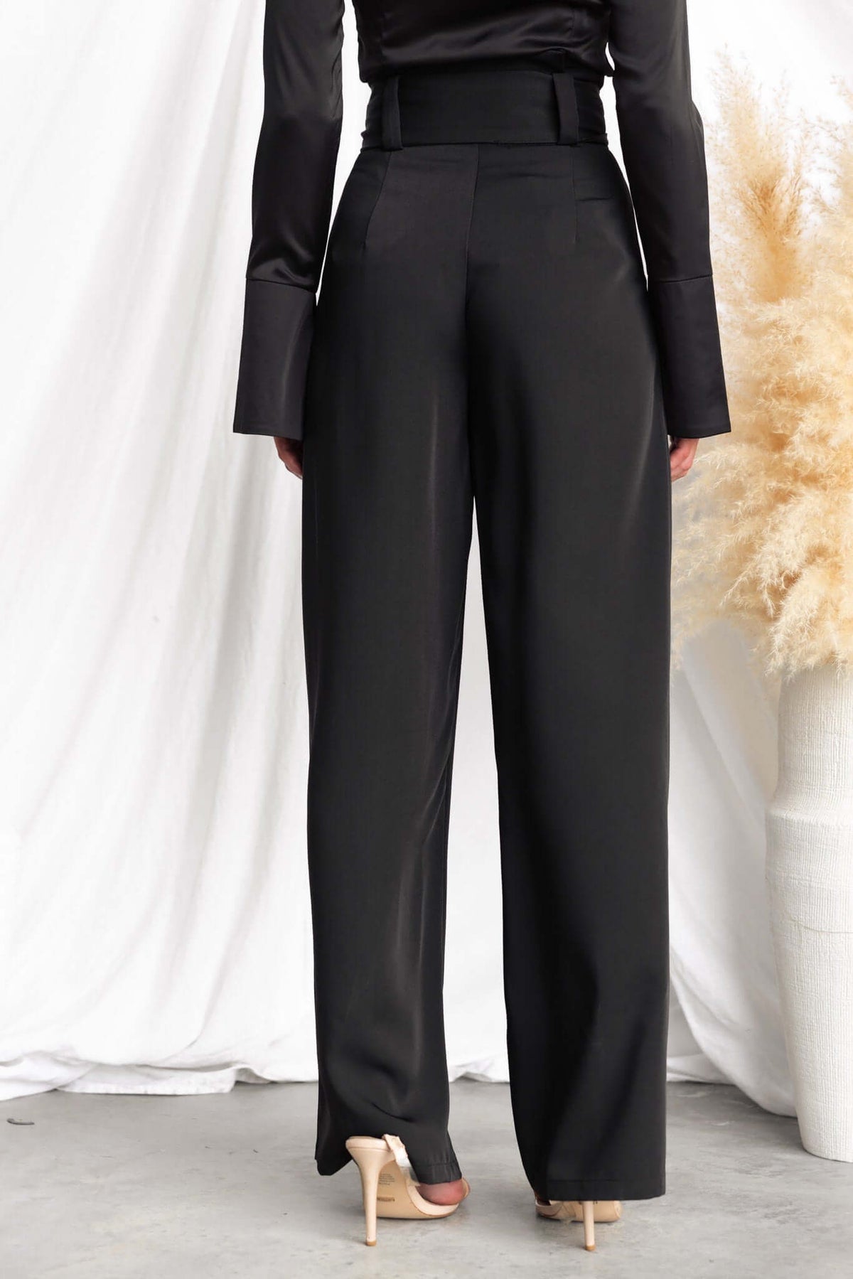Back view of Jaspin Pants with a paper bag waist and wide legs, styled with a black top against a soft backdrop.