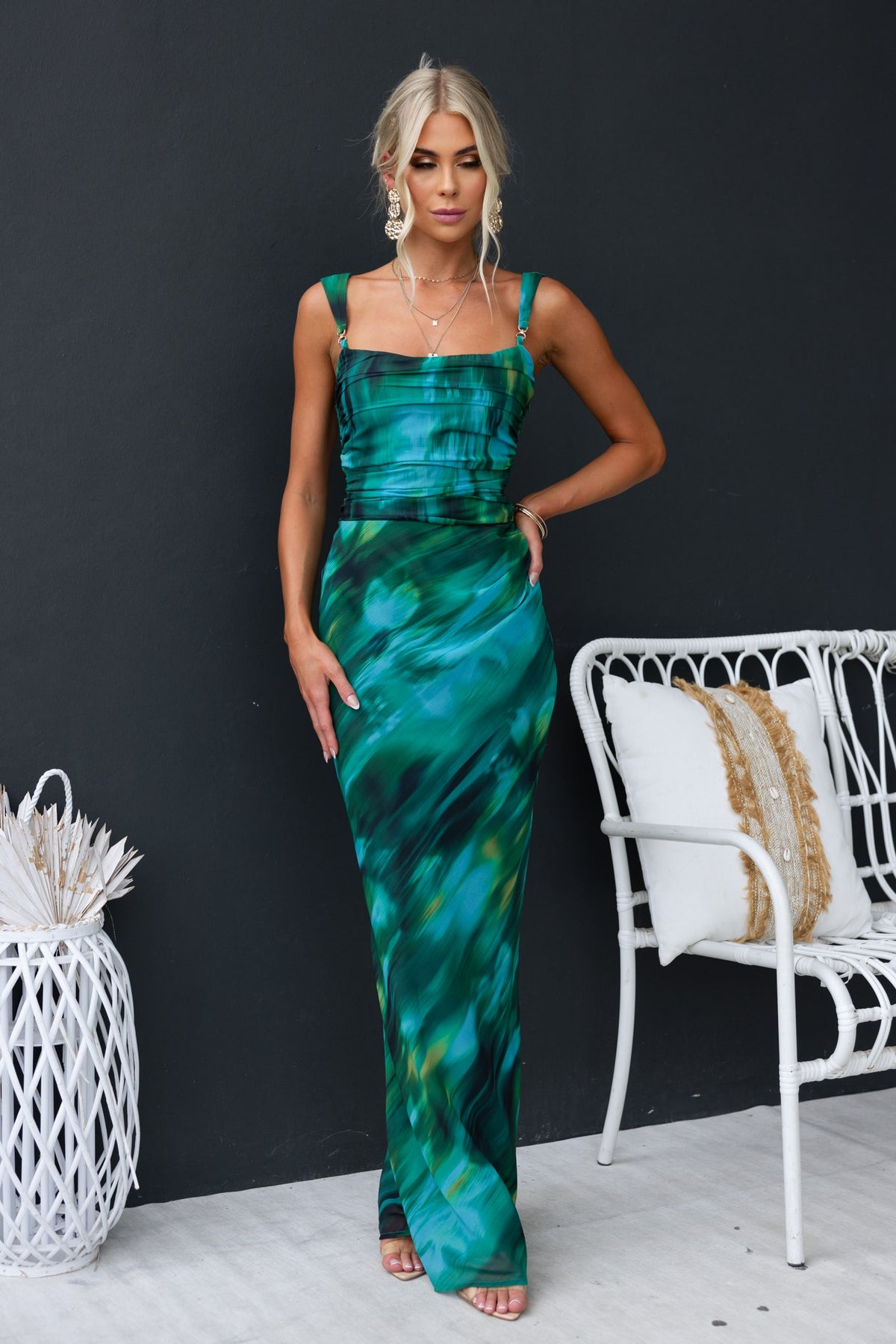 Model wearing the Voyage Maxi Dress with green print, gold hardware, and chiffon material against a dark backdrop.