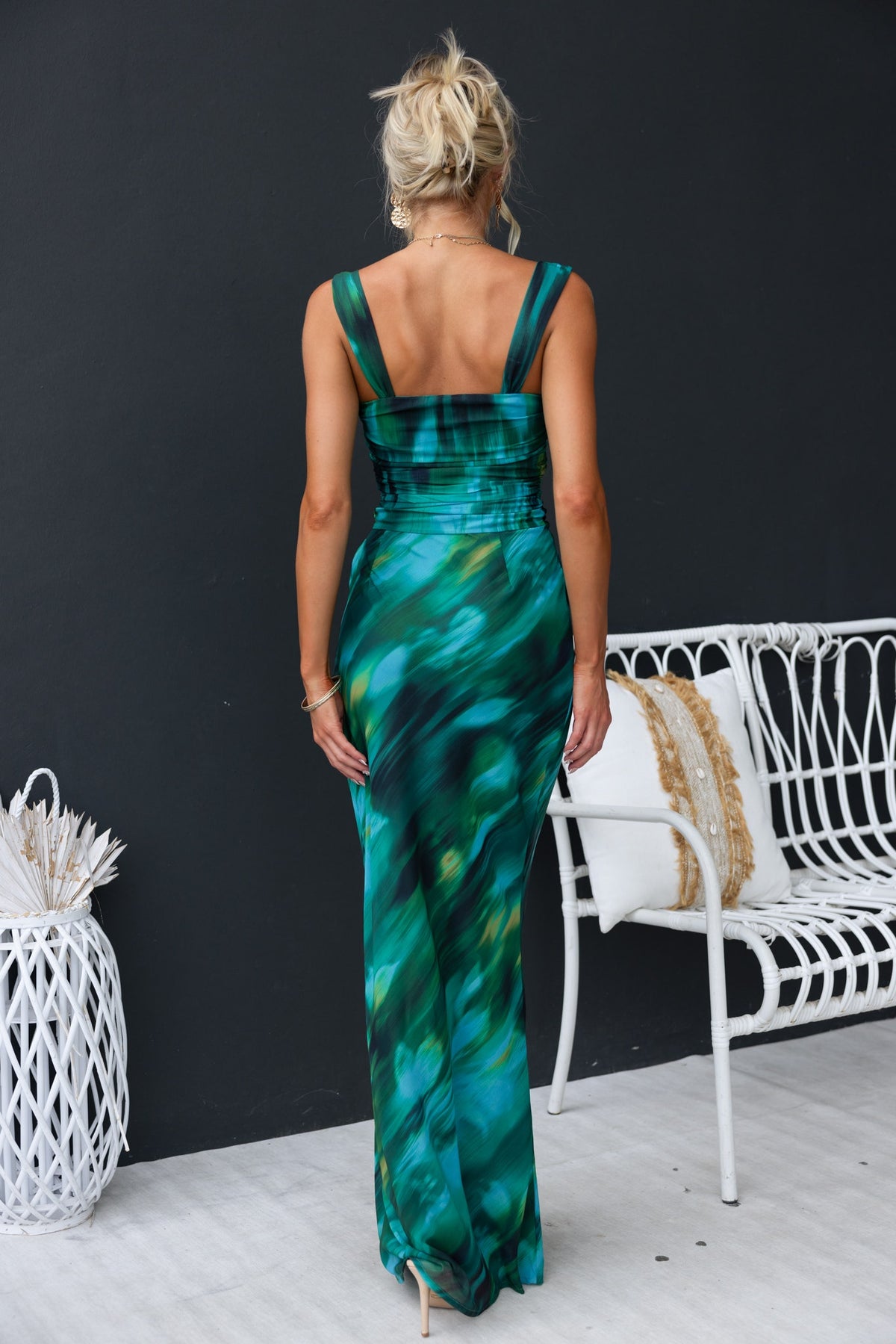 Rear view of a woman in a green printed Voyage Maxi Dress with gold hardware details, showcasing its chic design.