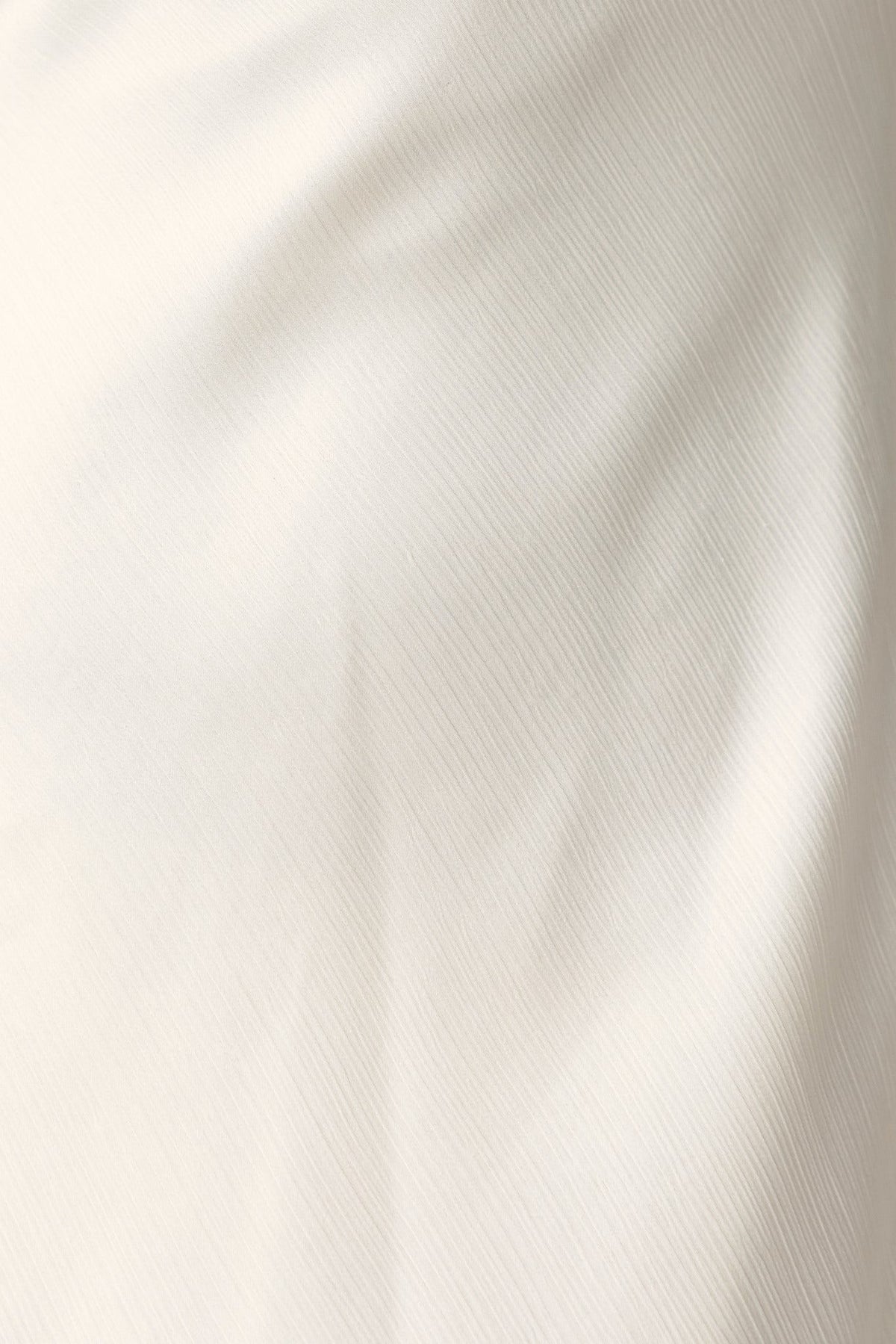 Lightly textured cream fabric of the Averi Dress, showcasing its fine details and quality material.