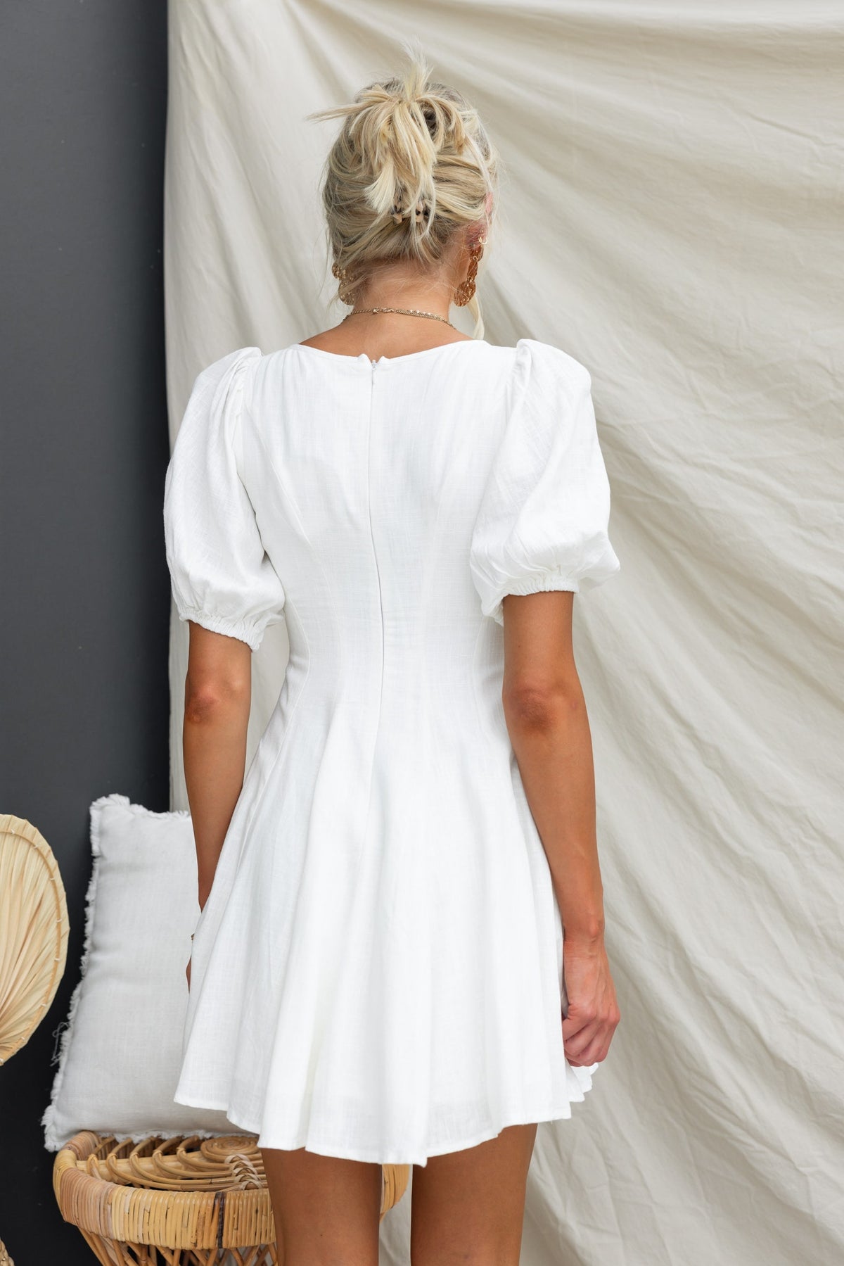 Back view of a white dress featuring puff sleeves and a fitted waist, styled with a relaxed hemline.