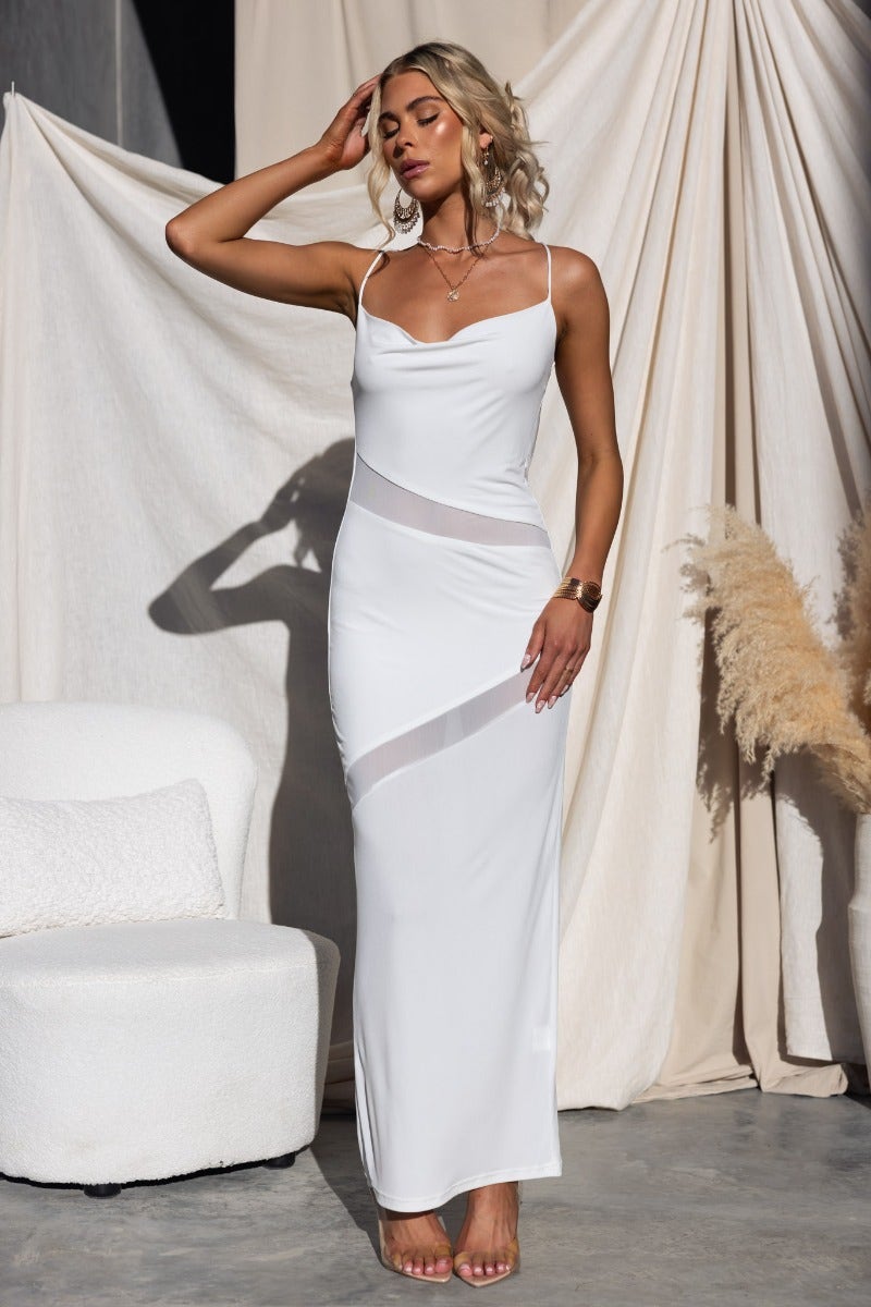 Millard Maxi Dress in white with cowl neckline, adjustable straps, and sheer panel details, styled with modern decor.