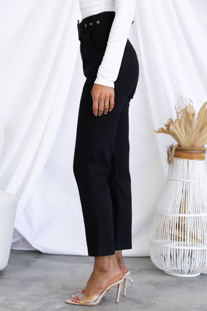 Side view of Kaniva black dress pants featuring a removable belt and pockets, styled with clear heels.