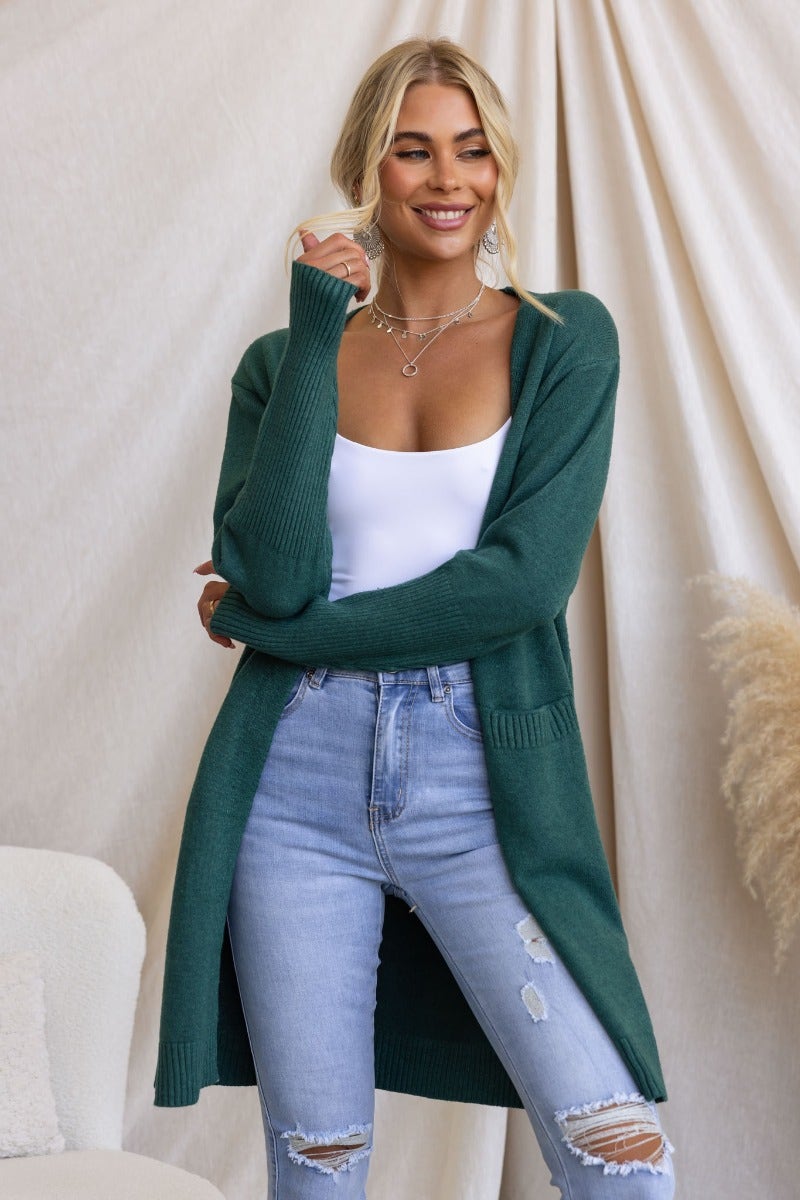 Model wearing a longline ribbed knit Motherly Cardigan in green, styled with ripped jeans and a white tank top.