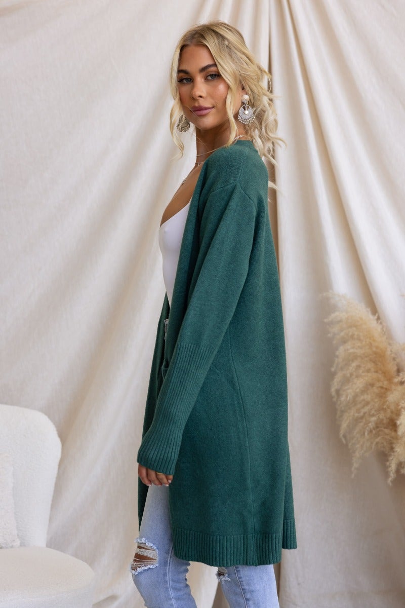 Model wearing a longline green ribbed knit cardigan with pockets, styled with a casual look.