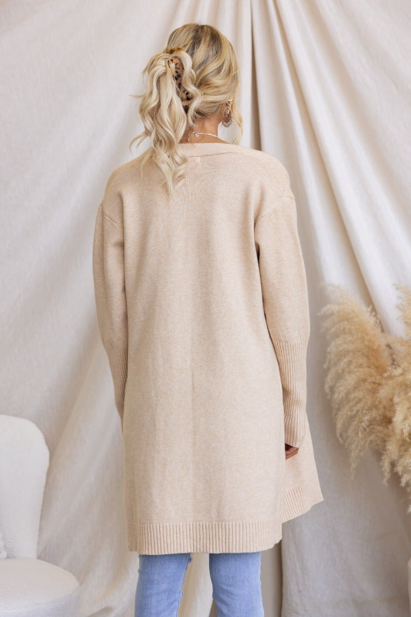 Back view of a woman wearing a beige ribbed knit longline cardigan with pockets, styled casually.