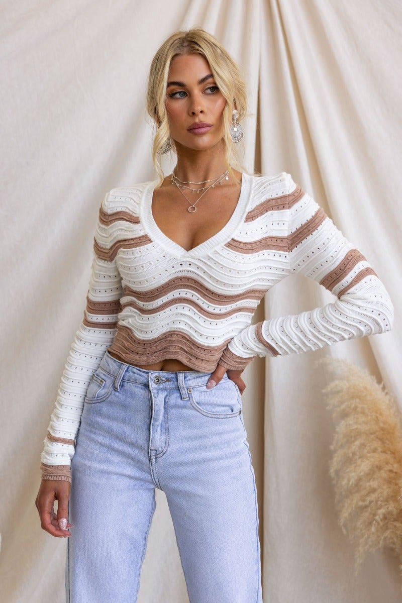 Model wearing Alanis Top, a semi open weave knit top with scoop neckline and wavy stripe design, styled with high-waisted jeans.
