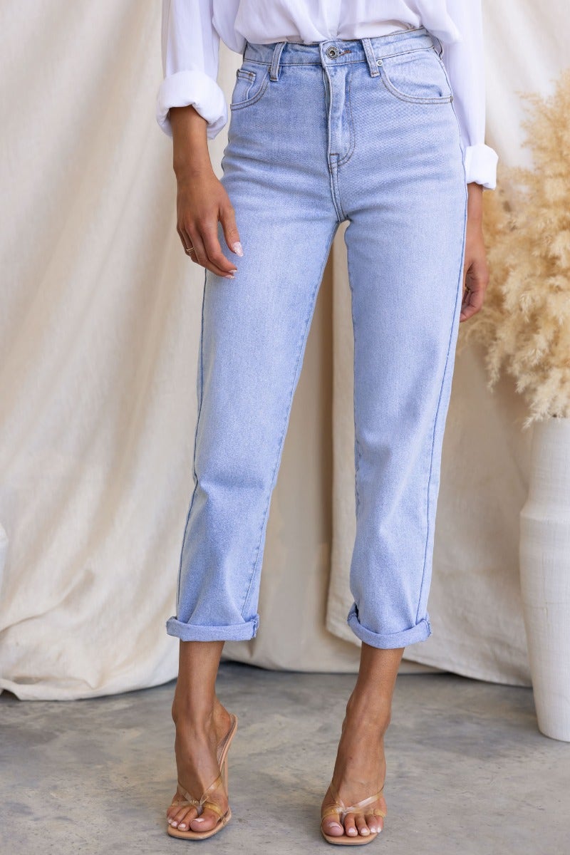 Light blue Isoka Jeans with mid-high waist and rolled cuffs, styled with a white blouse and minimalistic sandals.