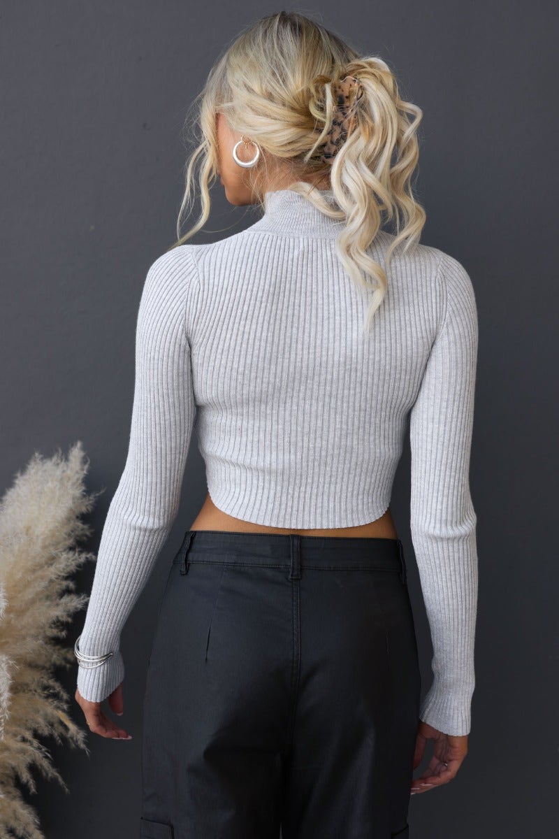 Back view of the Genova Top, a ribbed knit high neckline top with cut-outs, styled with black pants.