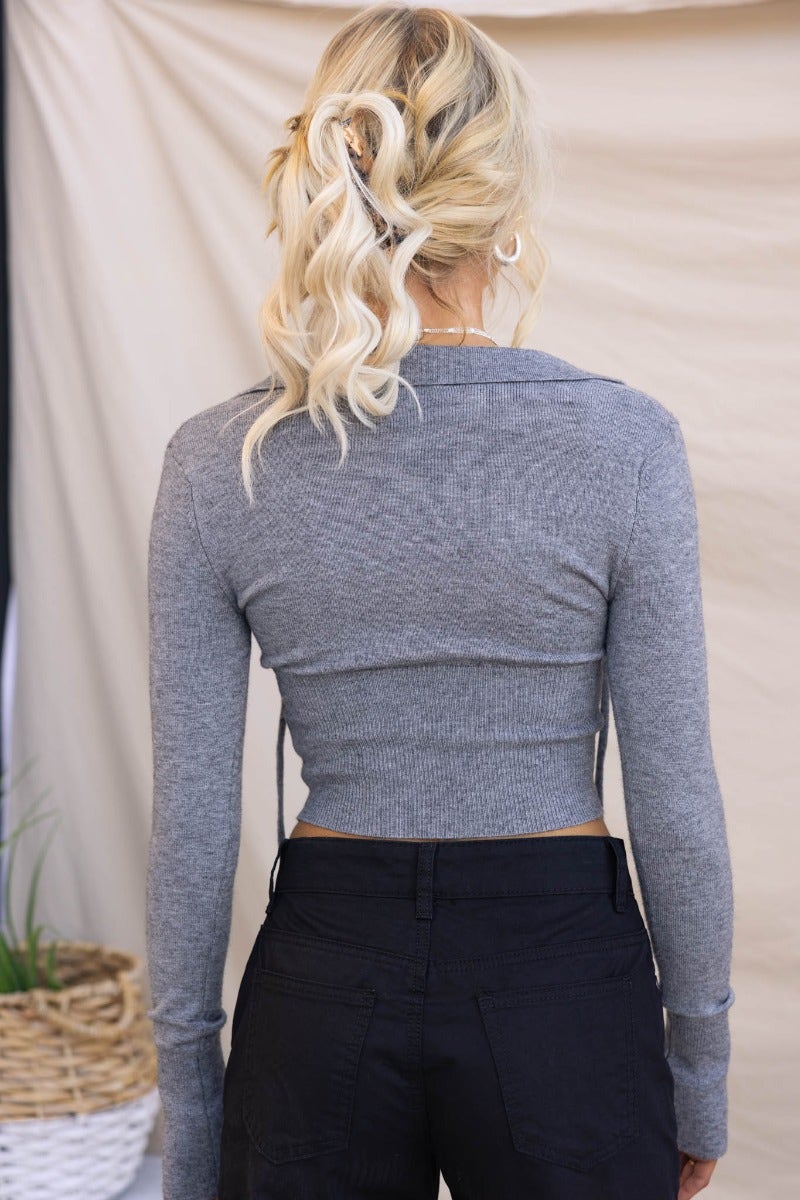 Back view of a model wearing a gray ribbed knit top with a collar and a tie detail, styled with black pants.
