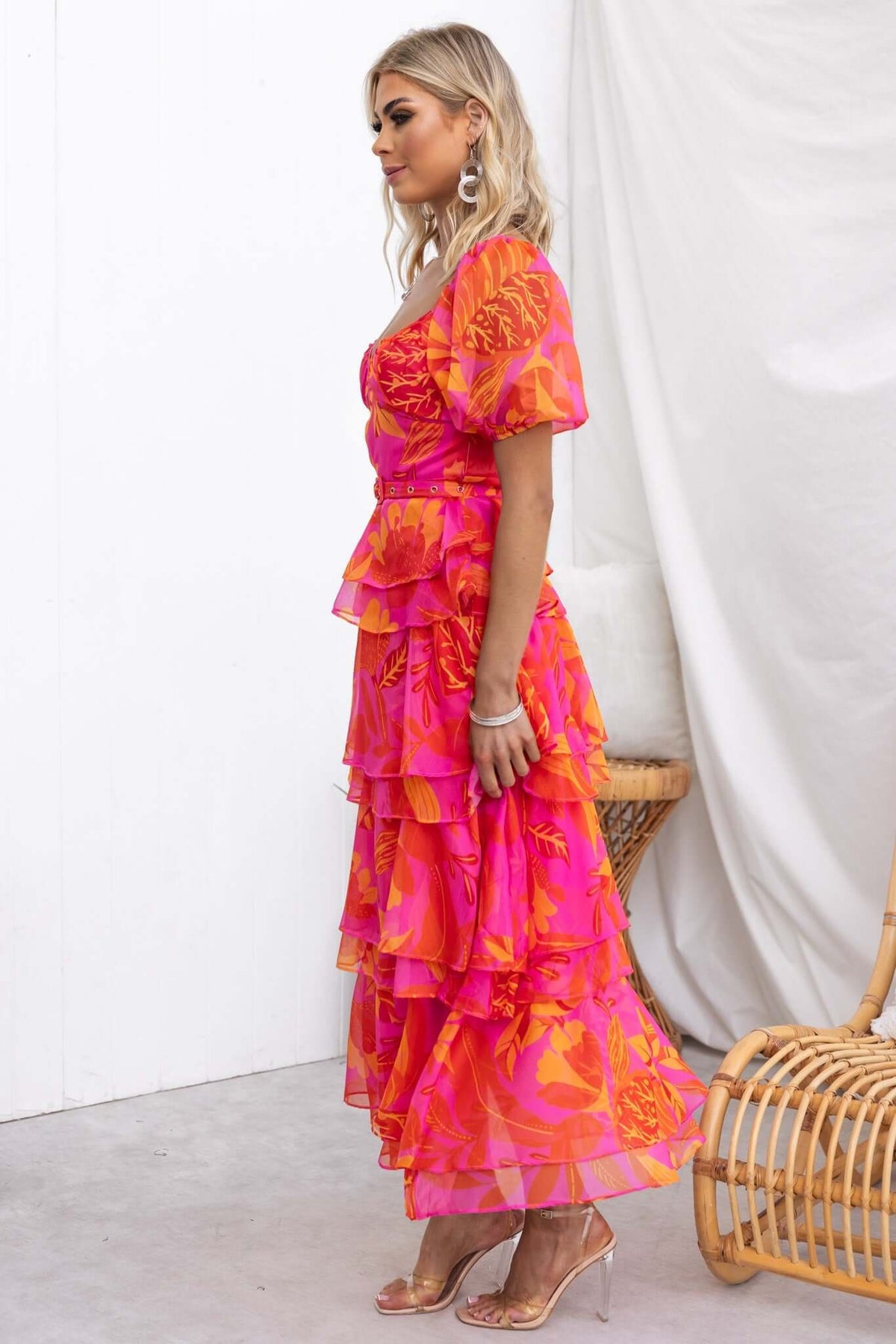 Model in a vibrant pink floral maxi dress with ruffle skirt and puff sleeves, showcasing stylish summer fashion.
