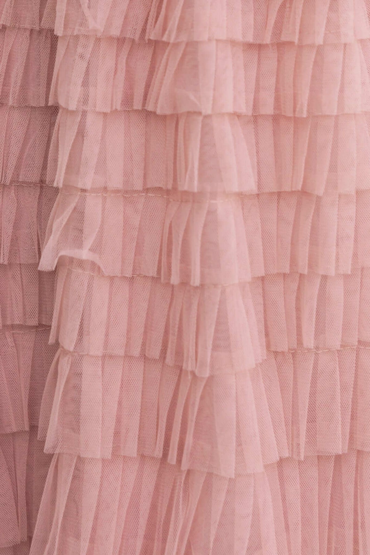 Close-up of layered tulle fabric in soft pink, showcasing ruffled texture for a feminine look.