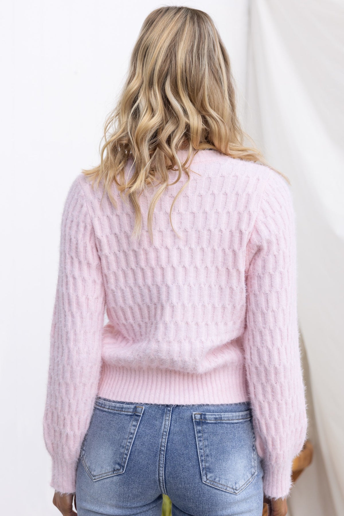 Back view of a woman wearing a soft pink Libra Jumper, featuring a round neckline and relaxed fit with a textured pattern.