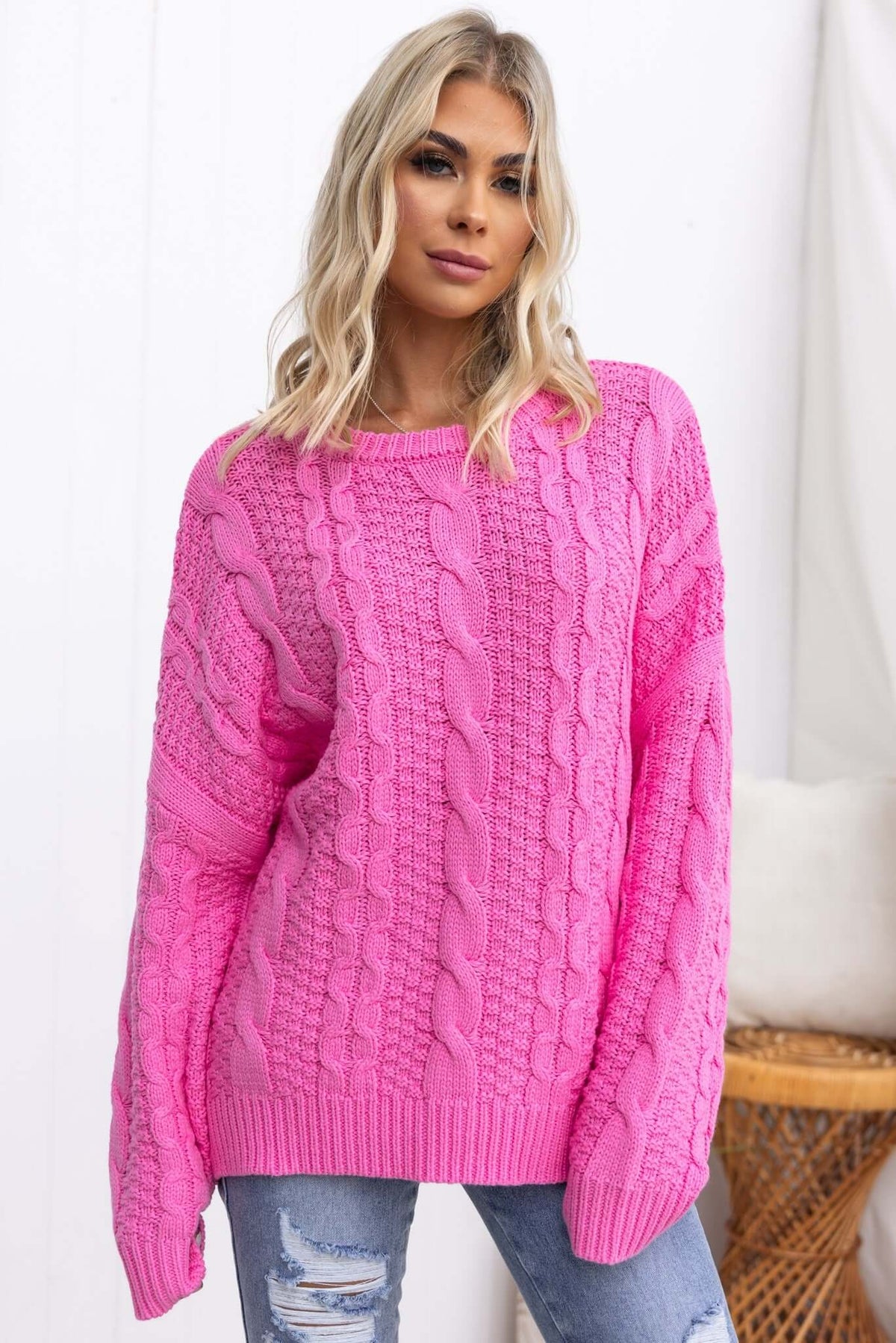 Varese Jumper in bright pink, featuring a round neckline and cable knit design, modeled by a woman with blonde hair.