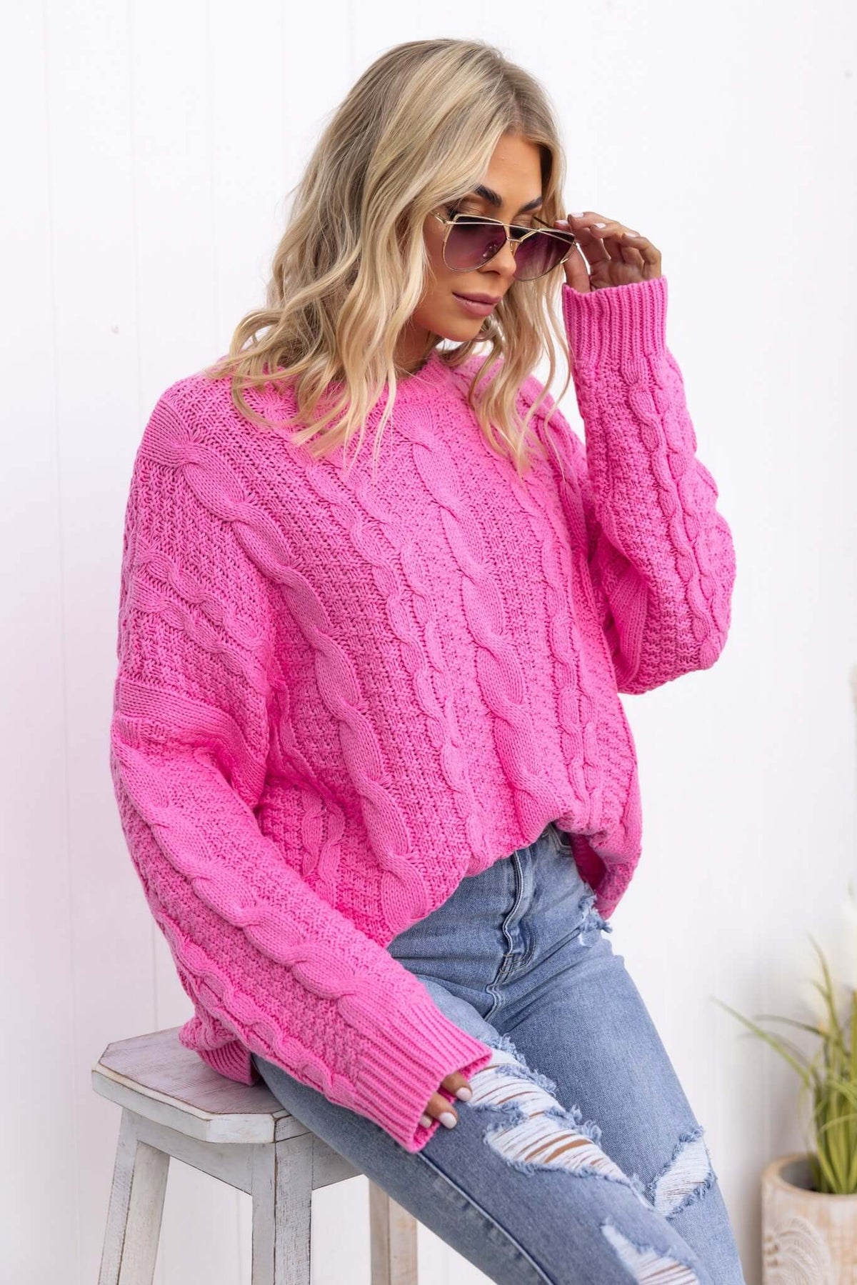 Varese Jumper in bright pink with cable knit design, styled with sunglasses and ripped jeans, perfect for casual fashion.