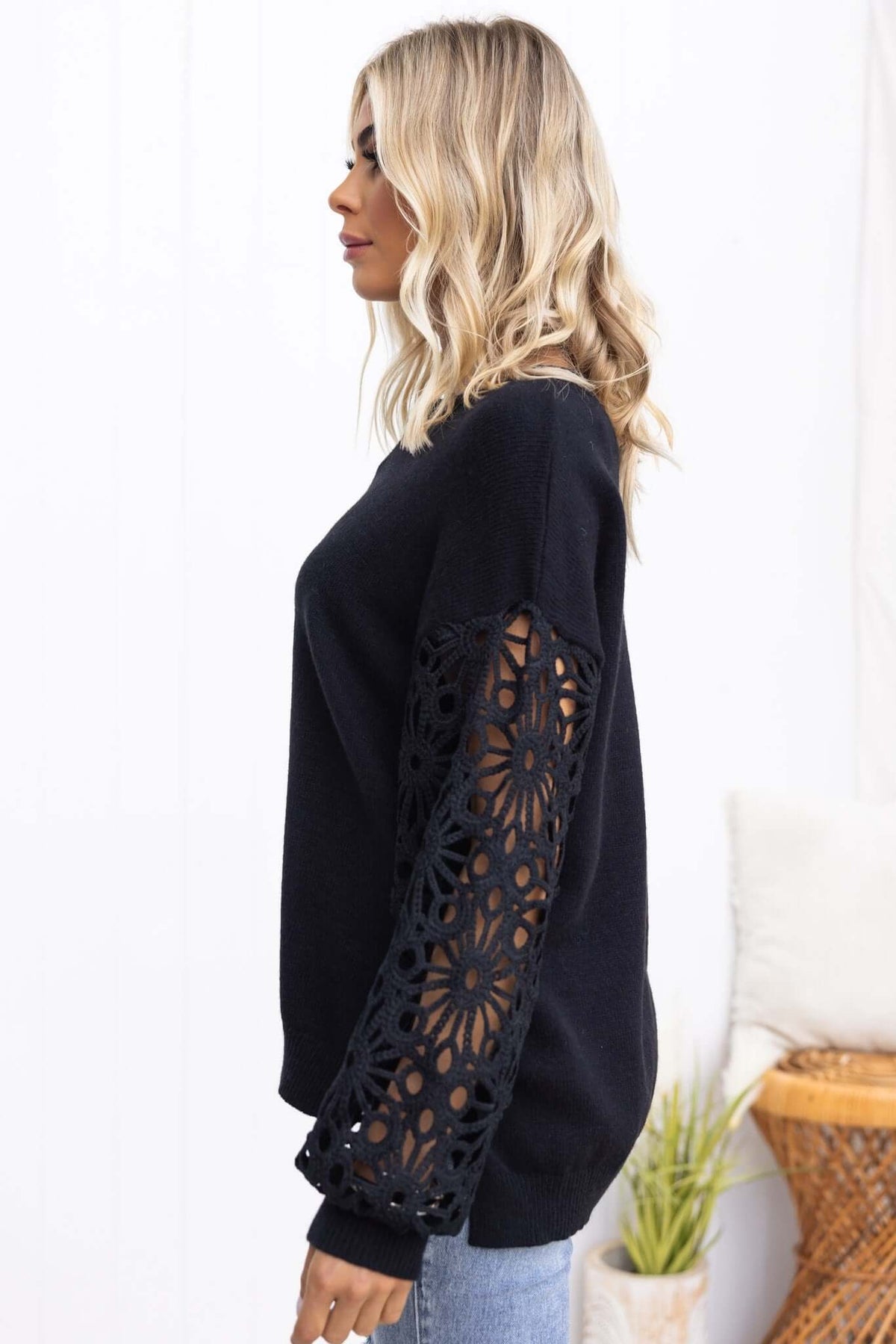 Side view of Mooney Jumper featuring black knit material and crochet sleeves, styled casually with light jeans.