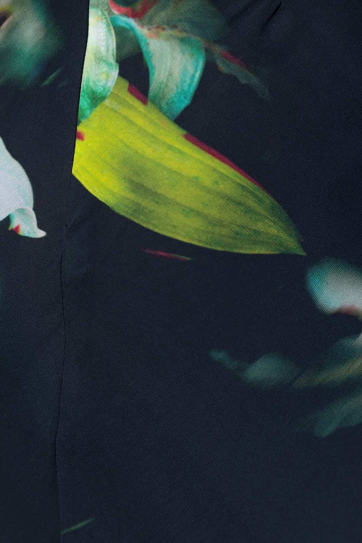 Close-up of a floral print on a black fabric, featuring bright green and white accents against a dark background.