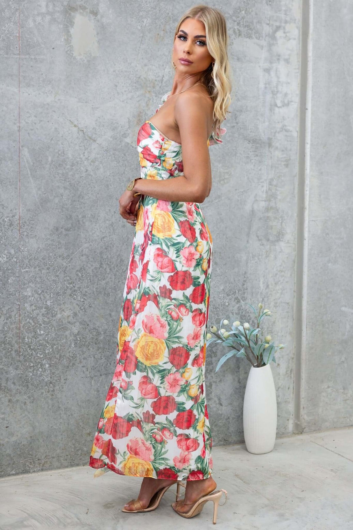 Model wearing Tresia Maxi Dress with floral design, showcasing one-shoulder neckline and front split against a gray background.