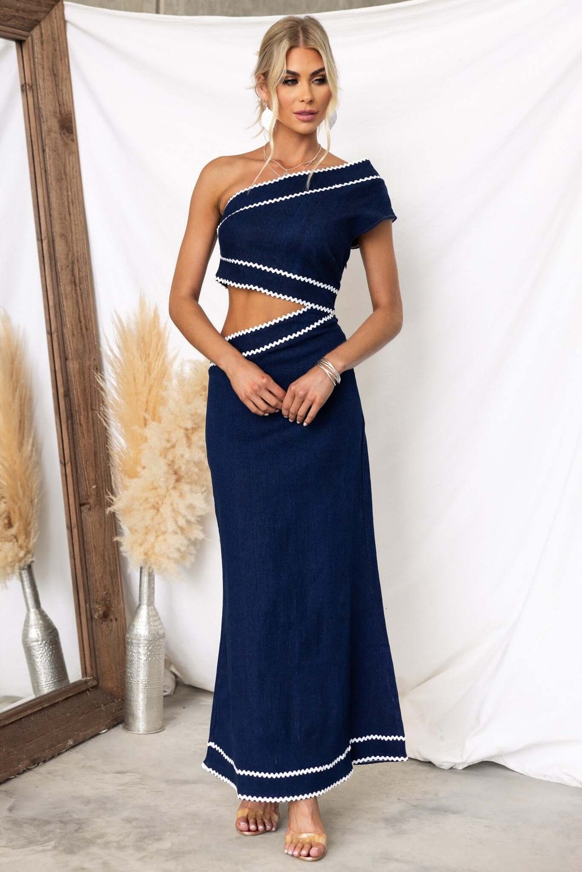 Favara Denim Maxi Dress in navy with one-shoulder style and cut-out waist detail, styled elegantly for a chic look.