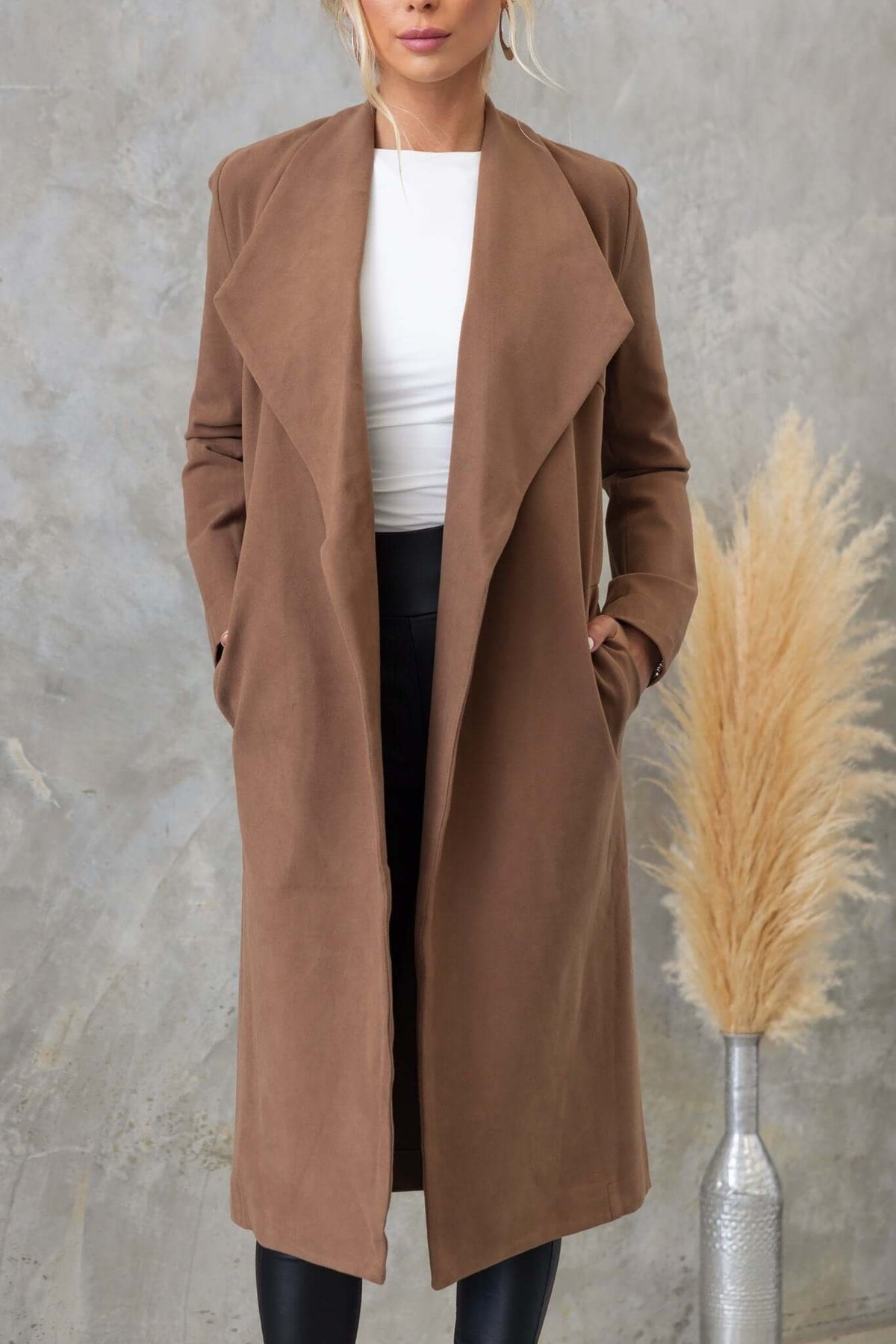 Aria longline coat in suede look with collar, lapels, and pockets, worn by model against a textured background.
