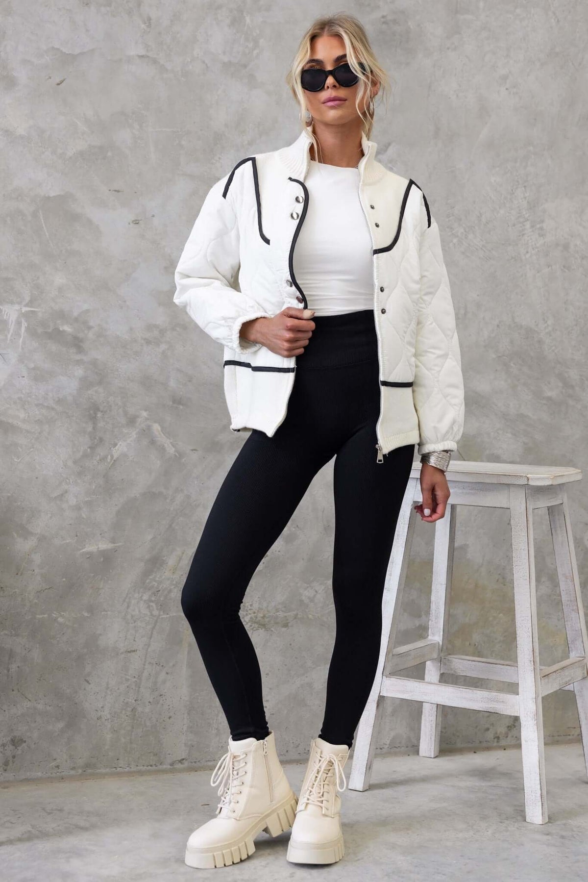 Model wearing the Carota Jacket, a high-neck, quilted jacket with pockets and elastic sleeves, styled with black leggings.