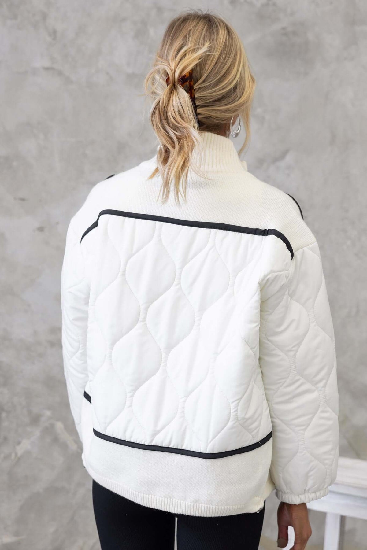 Back view of the Carota Jacket featuring quilted material, high neckline, and drawstring hem, styled with leggings.