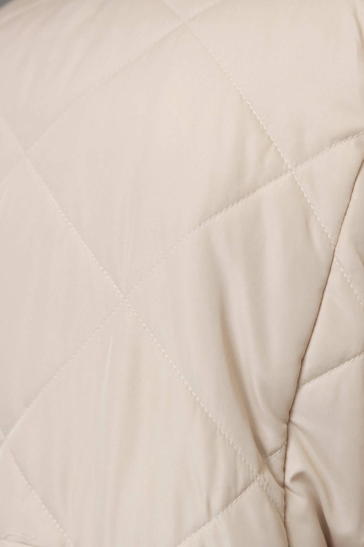 Close-up of the quilted fabric of the Chantel Coat, showcasing its soft beige texture and stylish design details.